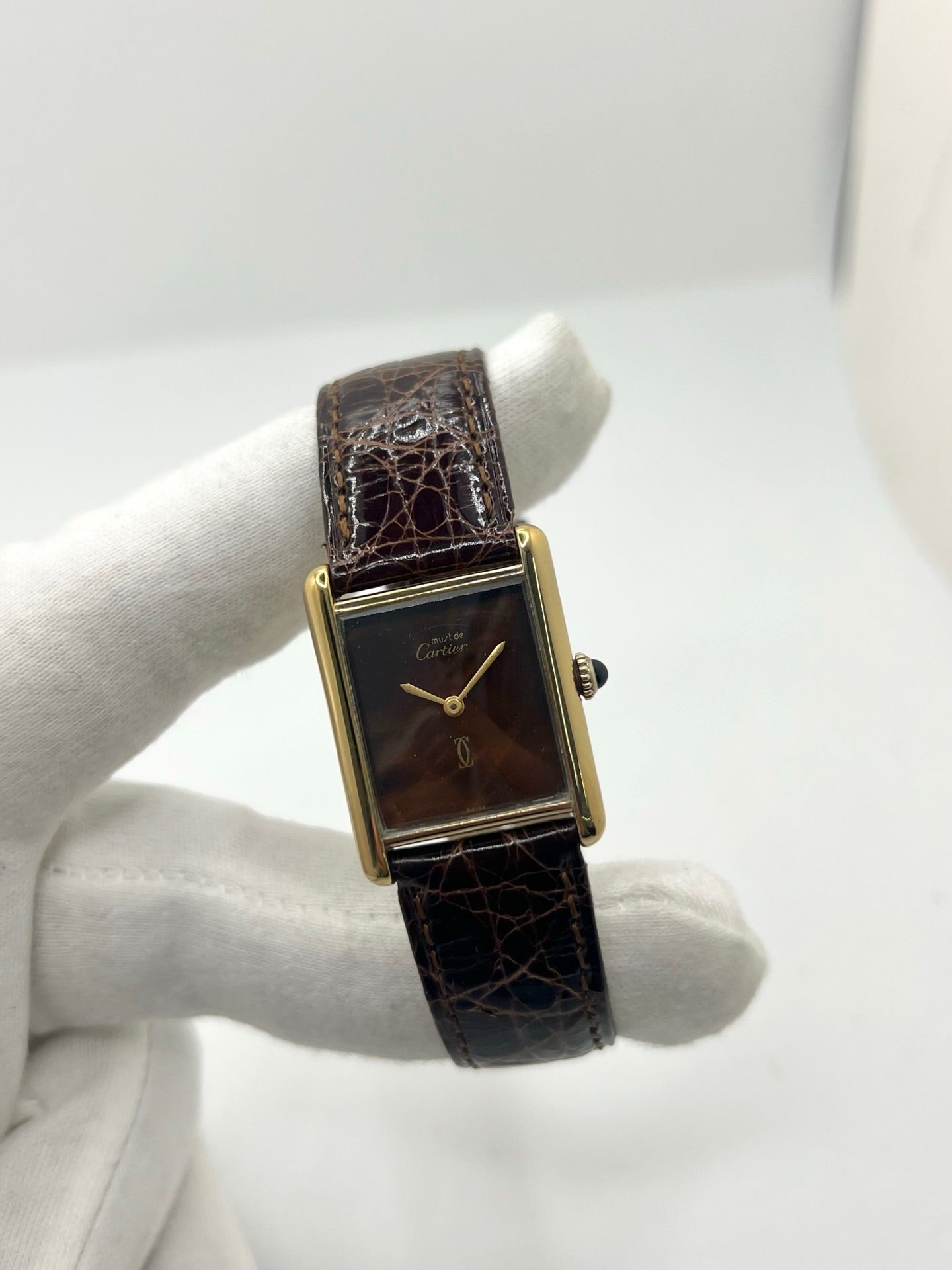Montre Cartier Tank Must Vermeil Œil de Tigre vintage avec boîtier rectangulaire en vermeil, mouvement à remontage manuel et cadran en pierre naturelle œil de tigre aux reflets bruns et dorés. Cette Cartier Must Tank Vermeil se distingue par son design emblématique, son bracelet en cuir brun et son élégance intemporelle. Montre de collection recherchée par les amateurs de montres Cartier vintage, alliant raffinement, caractère et savoir-faire horloger.