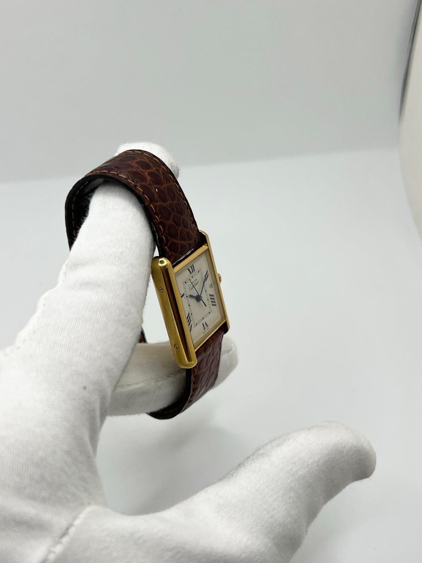 Montre Cartier Tank Must grand modèle en argent avec cadran blanc à chiffres romains, mouvement quartz et fonction date. Boîtier rectangulaire 25 x 33 mm avec verre minéral, bracelet en cuir brun et boucle ardillon en acier. Modèle iconique au design élégant et intemporel, idéal pour homme ou unisexe. Montre d’occasion en bon état, révisée, avec coffret d’origine.