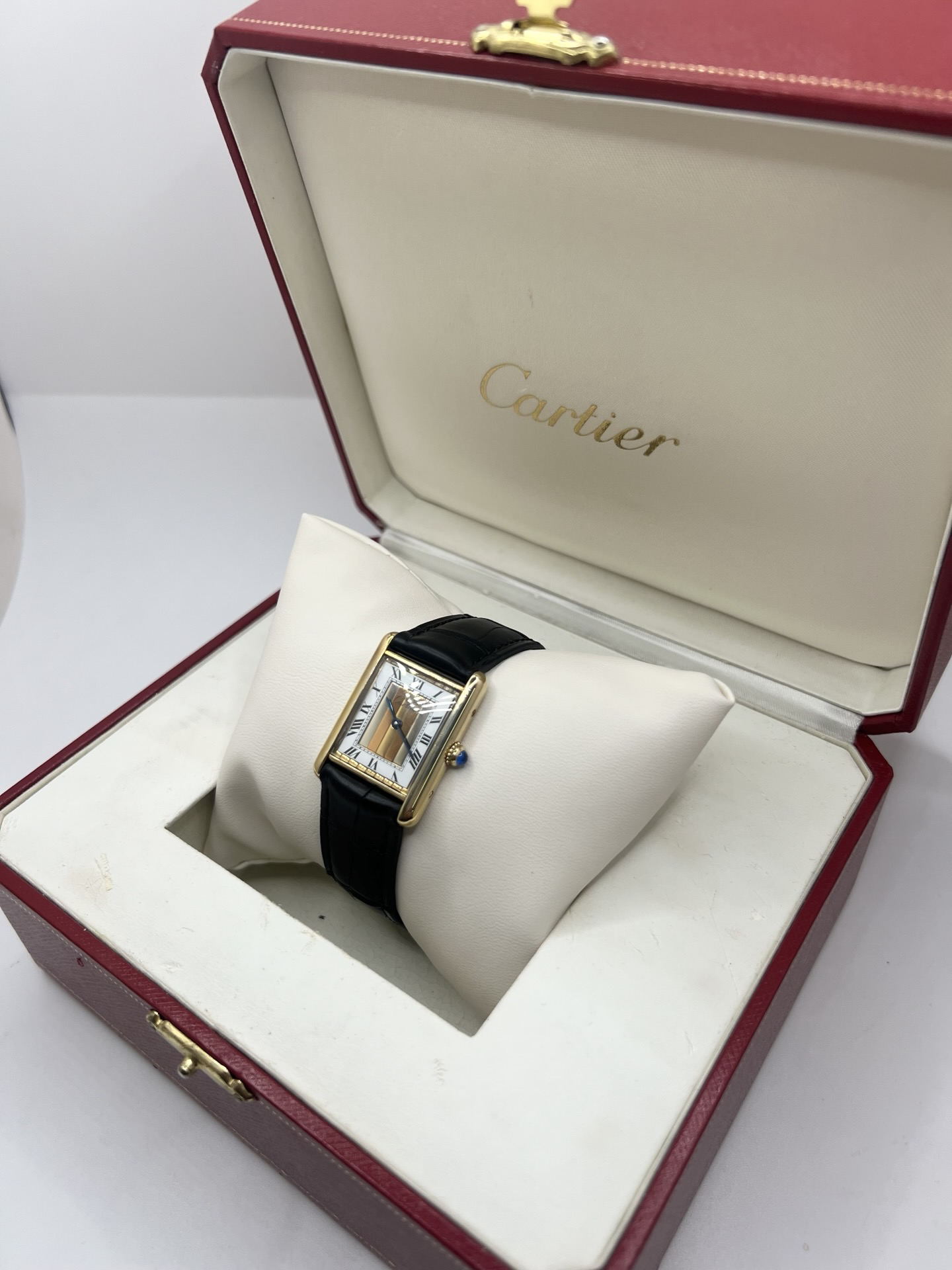 Montre Cartier Tank Must Trinity Grand Modèle vintage en vermeil, référence 590005, datant des années 1990. Boîtier rectangulaire de 23 x 30 mm en argent vermeil, cadran blanc à chiffres romains avec motif Trinity emblématique, verre saphir et mouvement quartz Cartier calibre 90. Bracelet en cuir avec boucle Cartier. Cette montre de luxe au design intemporel incarne l’élégance française et l’héritage horloger de Cartier, recherchée par les collectionneurs de montres vintage.