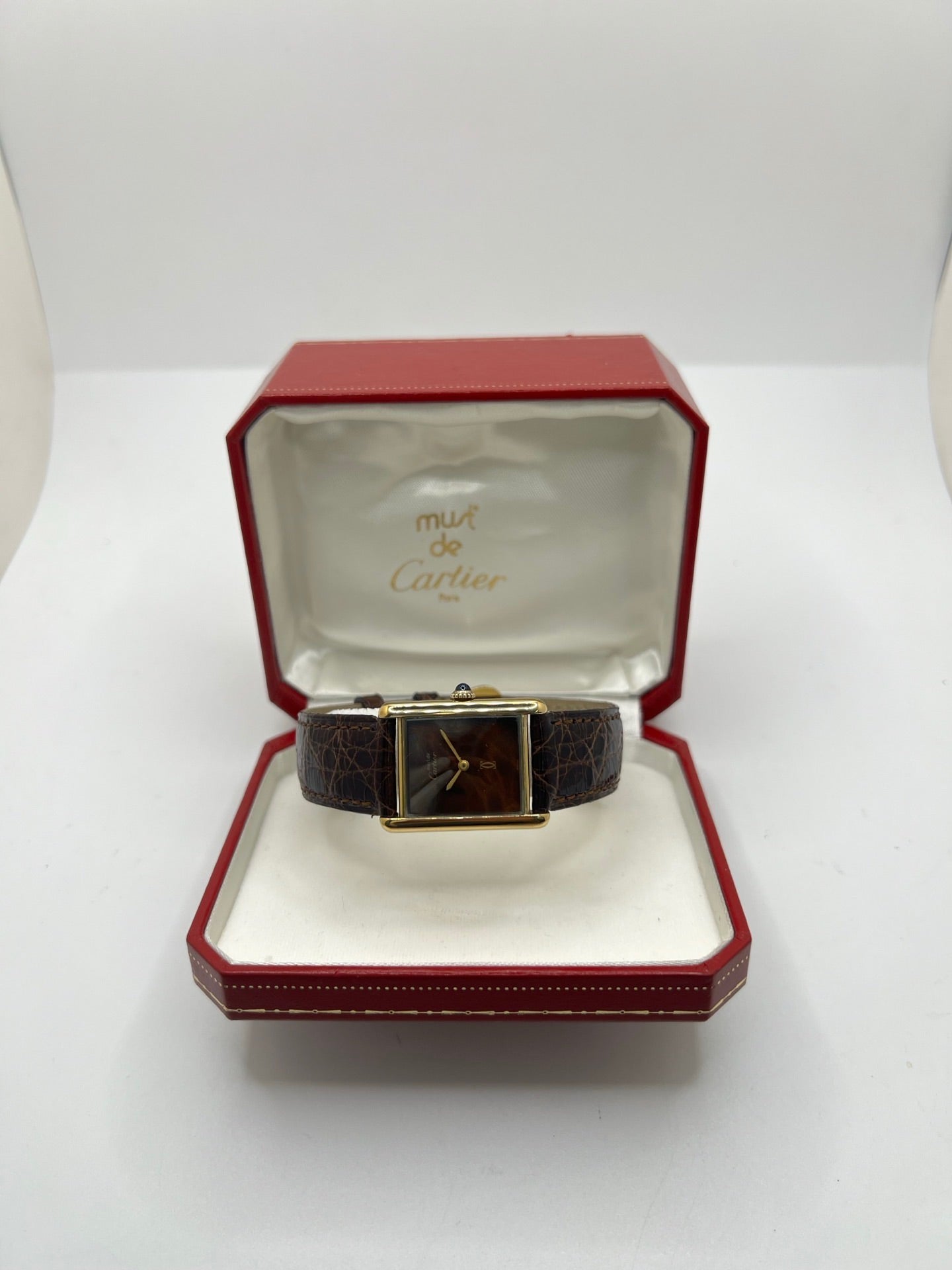 Montre Cartier Tank Must Vermeil Œil de Tigre vintage avec boîtier rectangulaire en vermeil, mouvement à remontage manuel et cadran en pierre naturelle œil de tigre aux reflets bruns et dorés. Cette Cartier Must Tank Vermeil se distingue par son design emblématique, son bracelet en cuir brun et son élégance intemporelle. Montre de collection recherchée par les amateurs de montres Cartier vintage, alliant raffinement, caractère et savoir-faire horloger.