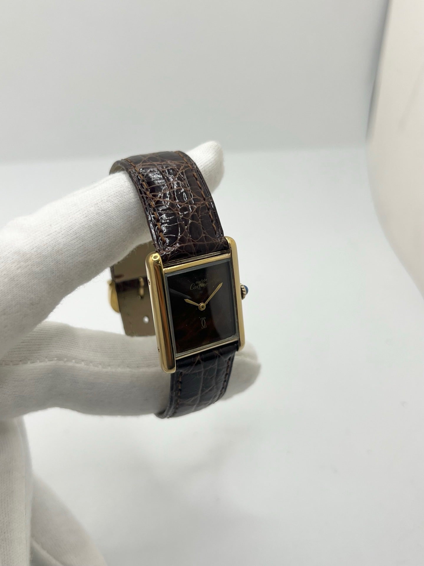 Montre Cartier Tank Must Vermeil Œil de Tigre vintage avec boîtier rectangulaire en vermeil, mouvement à remontage manuel et cadran en pierre naturelle œil de tigre aux reflets bruns et dorés. Cette Cartier Must Tank Vermeil se distingue par son design emblématique, son bracelet en cuir brun et son élégance intemporelle. Montre de collection recherchée par les amateurs de montres Cartier vintage, alliant raffinement, caractère et savoir-faire horloger.