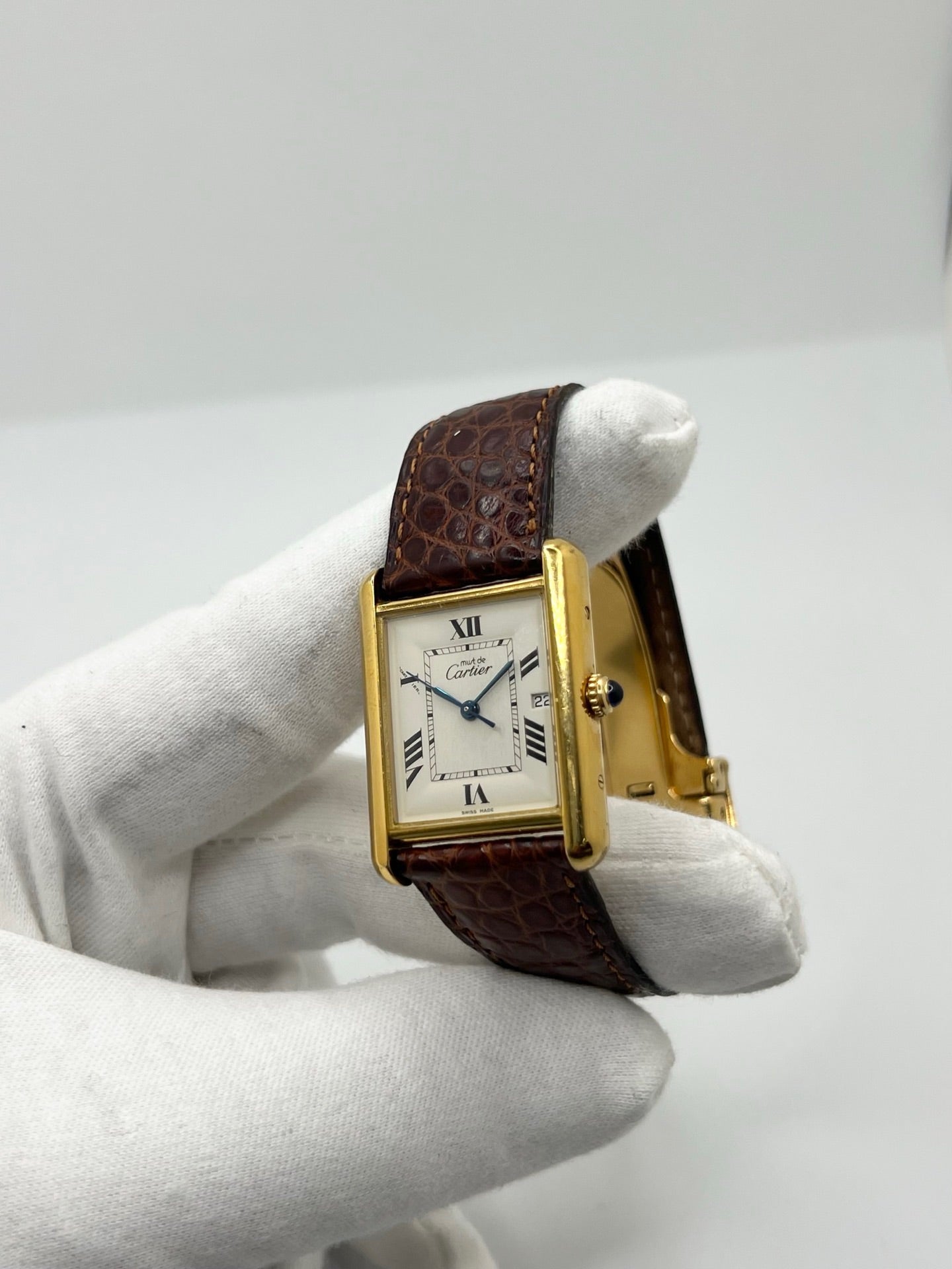 Montre Cartier Tank Must grand modèle en argent avec cadran blanc à chiffres romains, mouvement quartz et fonction date. Boîtier rectangulaire 25 x 33 mm avec verre minéral, bracelet en cuir brun et boucle ardillon en acier. Modèle iconique au design élégant et intemporel, idéal pour homme ou unisexe. Montre d’occasion en bon état, révisée, avec coffret d’origine.