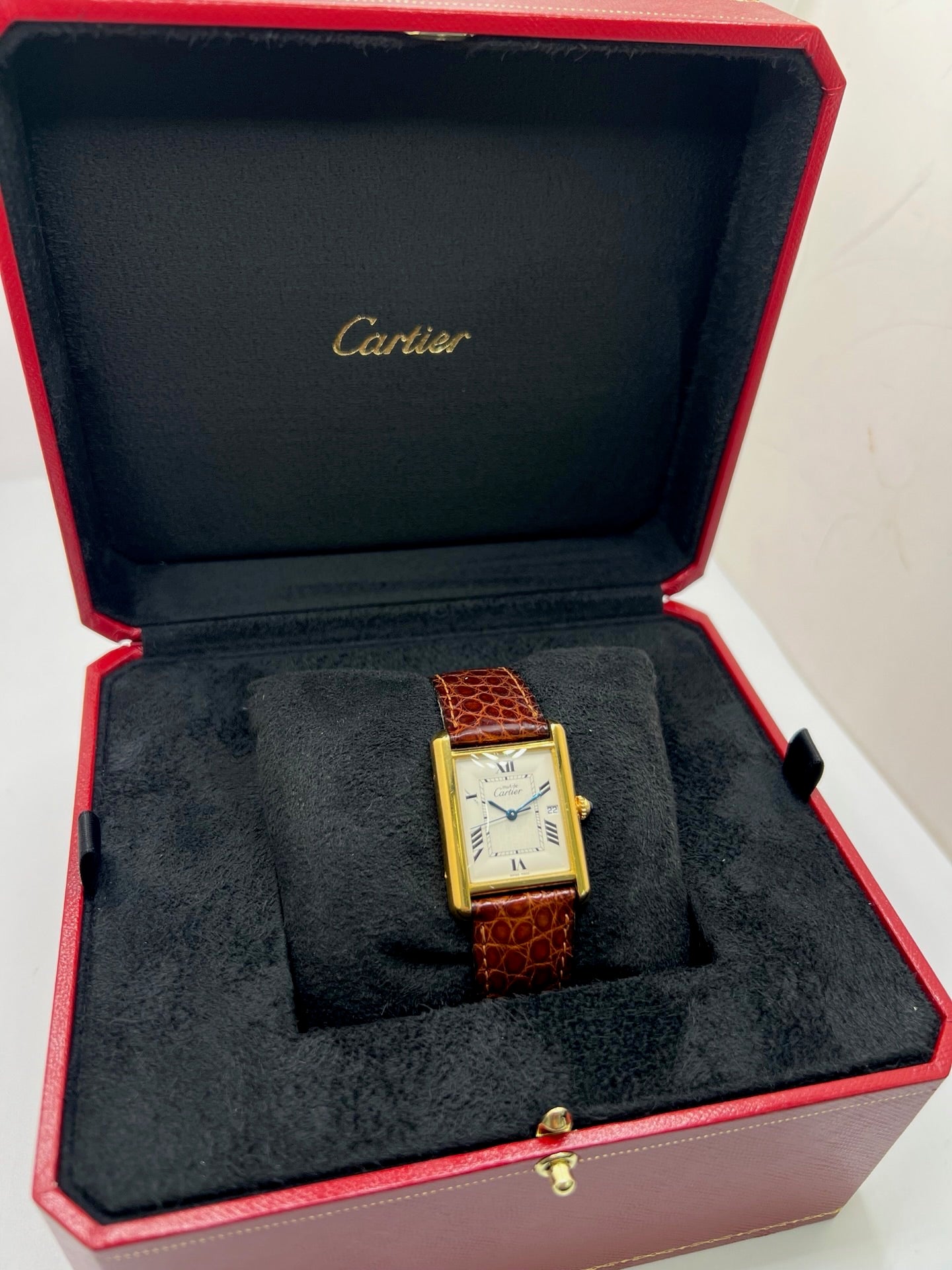 Montre Cartier Tank Must grand modèle en argent avec cadran blanc à chiffres romains, mouvement quartz et fonction date. Boîtier rectangulaire 25 x 33 mm avec verre minéral, bracelet en cuir brun et boucle ardillon en acier. Modèle iconique au design élégant et intemporel, idéal pour homme ou unisexe. Montre d’occasion en bon état, révisée, avec coffret d’origine.