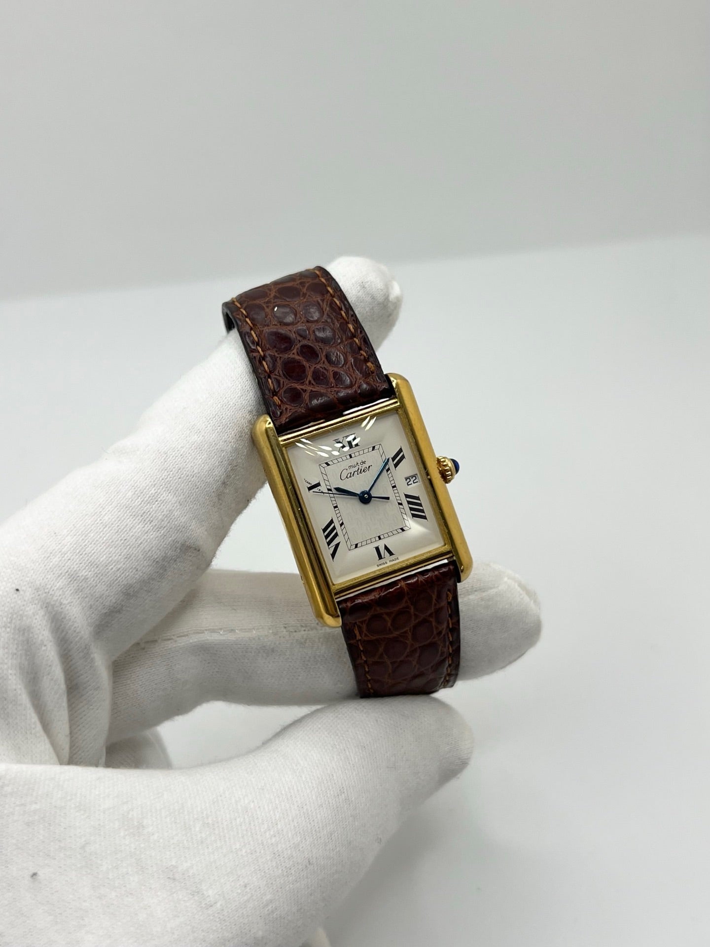 Montre Cartier Tank Must grand modèle en argent avec cadran blanc à chiffres romains, mouvement quartz et fonction date. Boîtier rectangulaire 25 x 33 mm avec verre minéral, bracelet en cuir brun et boucle ardillon en acier. Modèle iconique au design élégant et intemporel, idéal pour homme ou unisexe. Montre d’occasion en bon état, révisée, avec coffret d’origine.