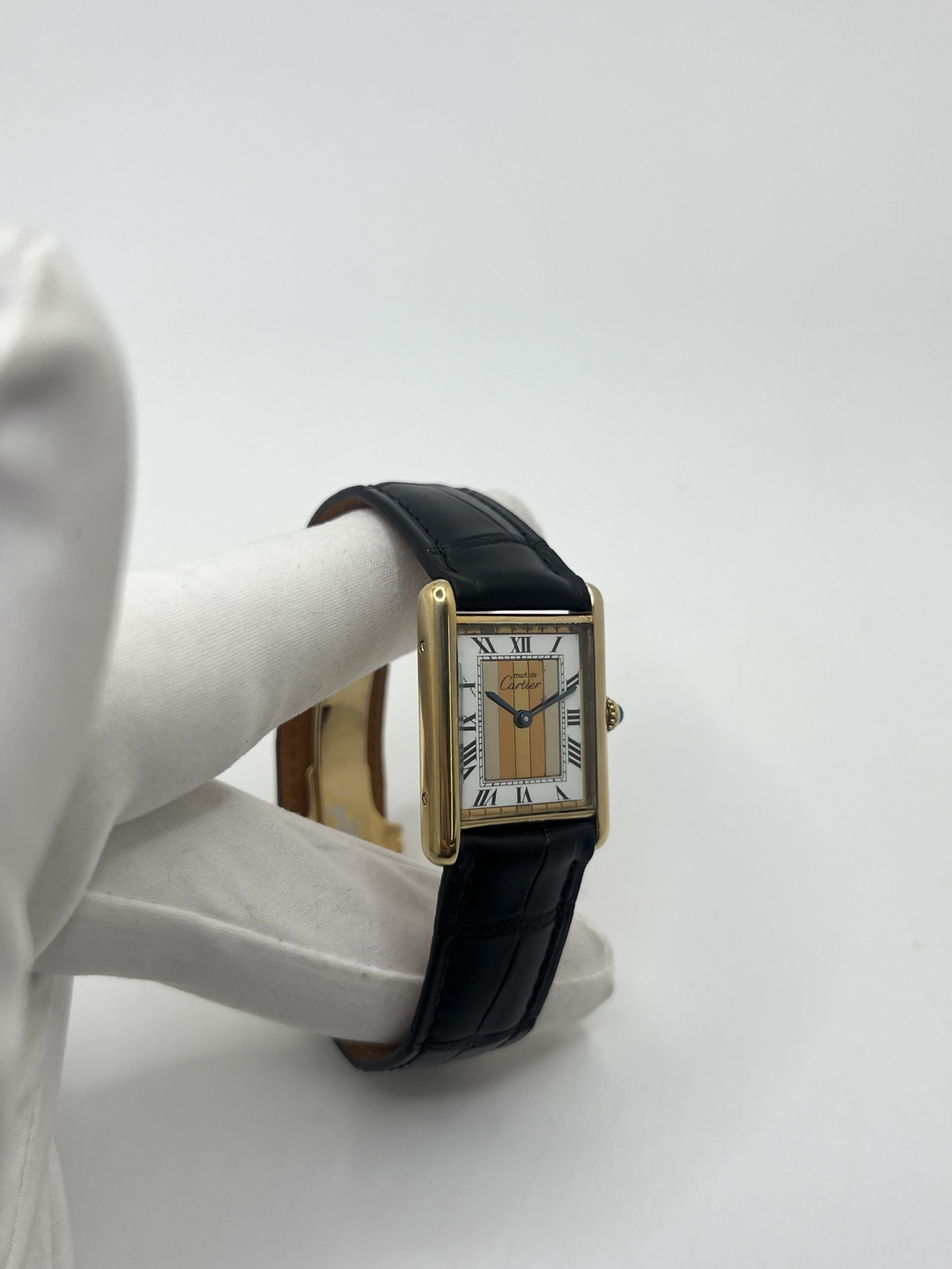 Montre Cartier Tank Must Trinity Grand Modèle vintage en vermeil, référence 590005, datant des années 1990. Boîtier rectangulaire de 23 x 30 mm en argent vermeil, cadran blanc à chiffres romains avec motif Trinity emblématique, verre saphir et mouvement quartz Cartier calibre 90. Bracelet en cuir avec boucle Cartier. Cette montre de luxe au design intemporel incarne l’élégance française et l’héritage horloger de Cartier, recherchée par les collectionneurs de montres vintage.