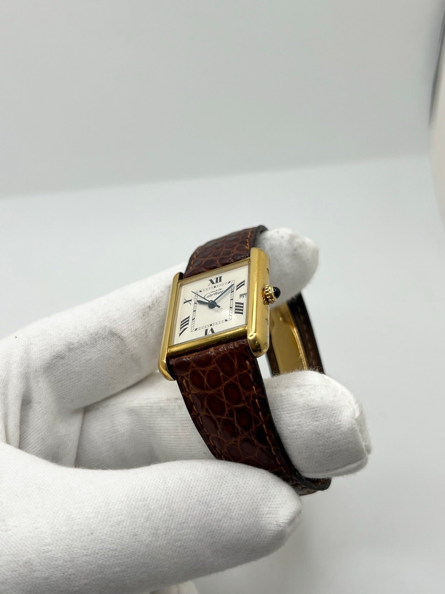 Montre Cartier Tank Must grand modèle en argent avec cadran blanc à chiffres romains, mouvement quartz et fonction date. Boîtier rectangulaire 25 x 33 mm avec verre minéral, bracelet en cuir brun et boucle ardillon en acier. Modèle iconique au design élégant et intemporel, idéal pour homme ou unisexe. Montre d’occasion en bon état, révisée, avec coffret d’origine.
