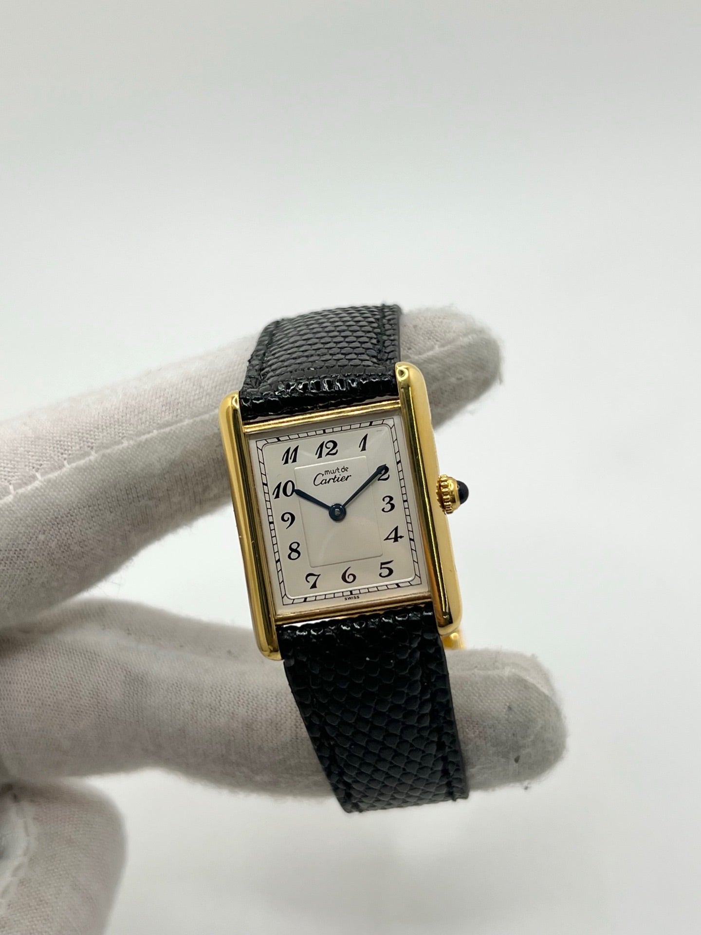 Montre Cartier Tank Vermeil référence 590005 vintage de 1989, avec boîtier rectangulaire en argent aux proportions classiques 23 x 30 mm, cadran argenté élégant avec chiffres arabes noirs et aiguilles bleuies, verre saphir et mouvement quartz. Montée sur un bracelet en cuir de lézard noir avec boucle ardillon en acier. Modèle iconique au design intemporel, livré avec son coffret et ses papiers d’origine, en très bon état.