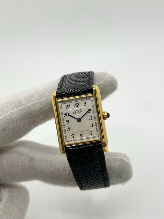 Montre Cartier Tank Vermeil référence 590005 vintage de 1989, avec boîtier rectangulaire en argent aux proportions classiques 23 x 30 mm, cadran argenté élégant avec chiffres arabes noirs et aiguilles bleuies, verre saphir et mouvement quartz. Montée sur un bracelet en cuir de lézard noir avec boucle ardillon en acier. Modèle iconique au design intemporel, livré avec son coffret et ses papiers d’origine, en très bon état.