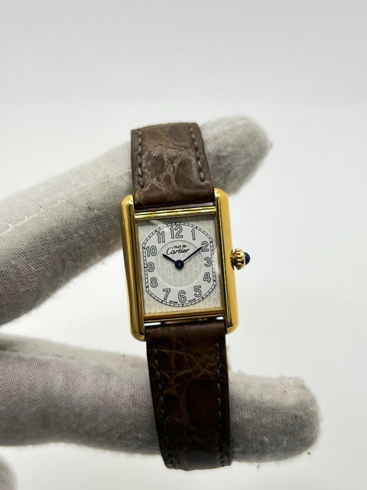 Montre Cartier Tank Vermeil 2415 pour femme, équipée d’un mouvement quartz et d’un boîtier en argent de 22 x 29 mm. Ce modèle d’occasion en bon état présente des traces d’usure visibles, un cadran blanc à chiffres arabes, un verre minéral et un bracelet en cuir brun avec boucle ardillon en argent. Élégante et classique, la Cartier Tank Vermeil 2415 séduit par son design intemporel, idéale pour les passionnées de montres de luxe.