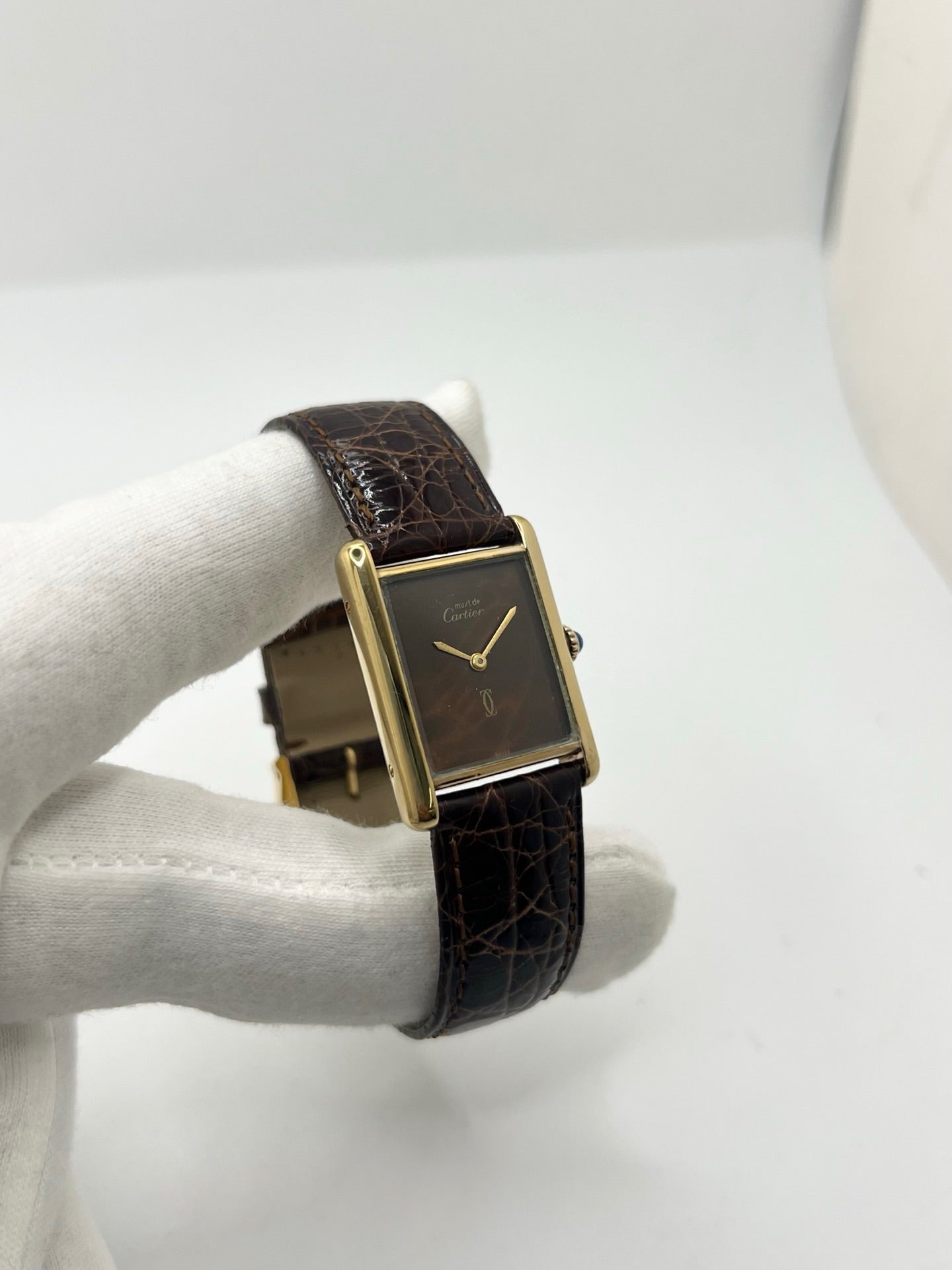 Montre Cartier Tank Must Vermeil Œil de Tigre vintage avec boîtier rectangulaire en vermeil, mouvement à remontage manuel et cadran en pierre naturelle œil de tigre aux reflets bruns et dorés. Cette Cartier Must Tank Vermeil se distingue par son design emblématique, son bracelet en cuir brun et son élégance intemporelle. Montre de collection recherchée par les amateurs de montres Cartier vintage, alliant raffinement, caractère et savoir-faire horloger.