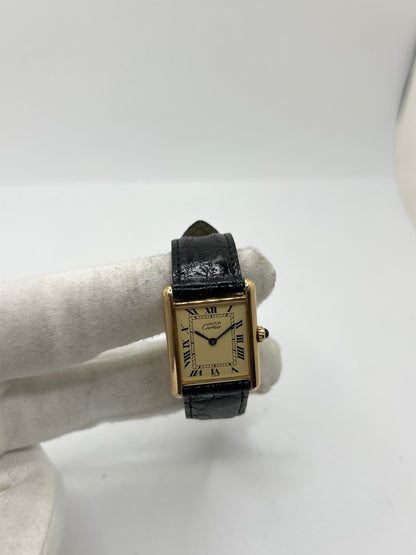 Montre Cartier Tank Vermeil réf. 590005 en argent avec mouvement à quartz, cadran champagne à chiffres romains et verre saphir. Ce modèle emblématique est monté sur un bracelet en cuir de crocodile noir avec boucle ardillon en acier. Son boîtier de 23 × 30 mm offre une élégance intemporelle. Cette montre Cartier Tank Vermeil d'occasion est en très bon état, révisée en interne et livrée avec son coffret d'origine.