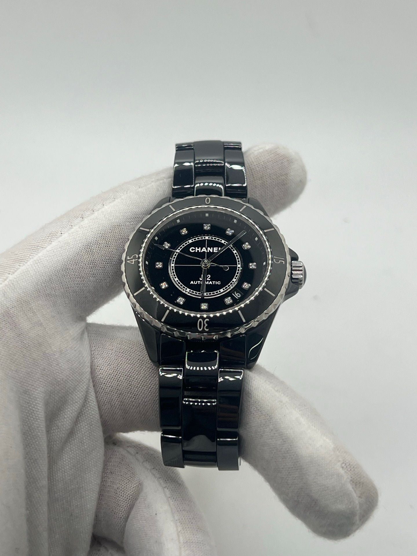 Montre Chanel J12 12.1 en céramique noire avec sertissage de diamants, alliant élégance et performance. Mouvement automatique de précision, boîtier de 38 mm et verre saphir. Modèle de luxe d'occasion en excellent état, livré avec coffret d'origine. Idéal pour collectionneurs et amateurs de haute horlogerie.