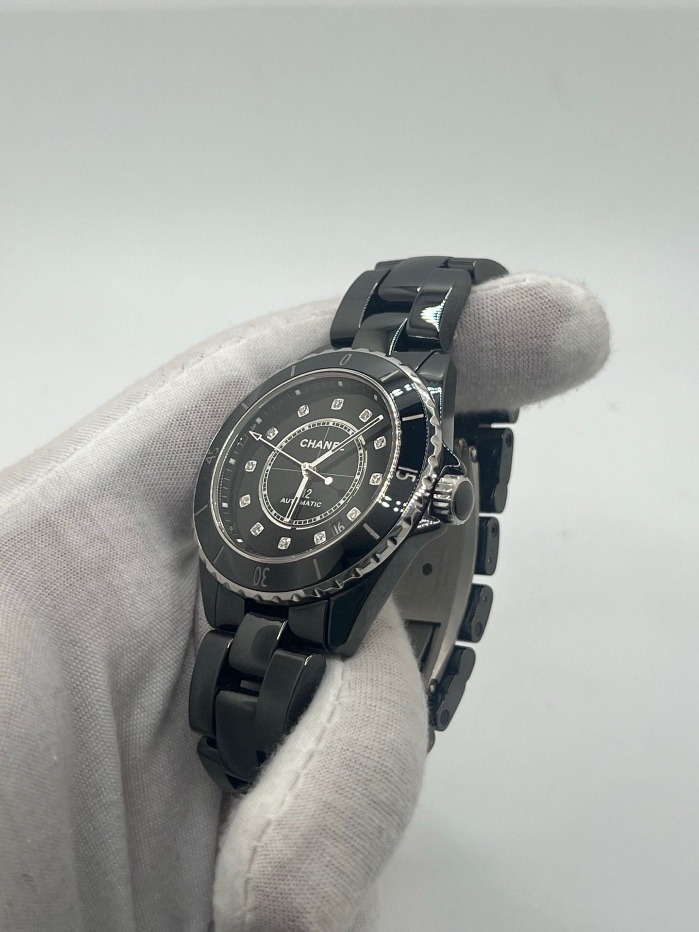 Montre Chanel J12 12.1 en céramique noire avec sertissage de diamants, alliant élégance et performance. Mouvement automatique de précision, boîtier de 38 mm et verre saphir. Modèle de luxe d'occasion en excellent état, livré avec coffret d'origine. Idéal pour collectionneurs et amateurs de haute horlogerie.