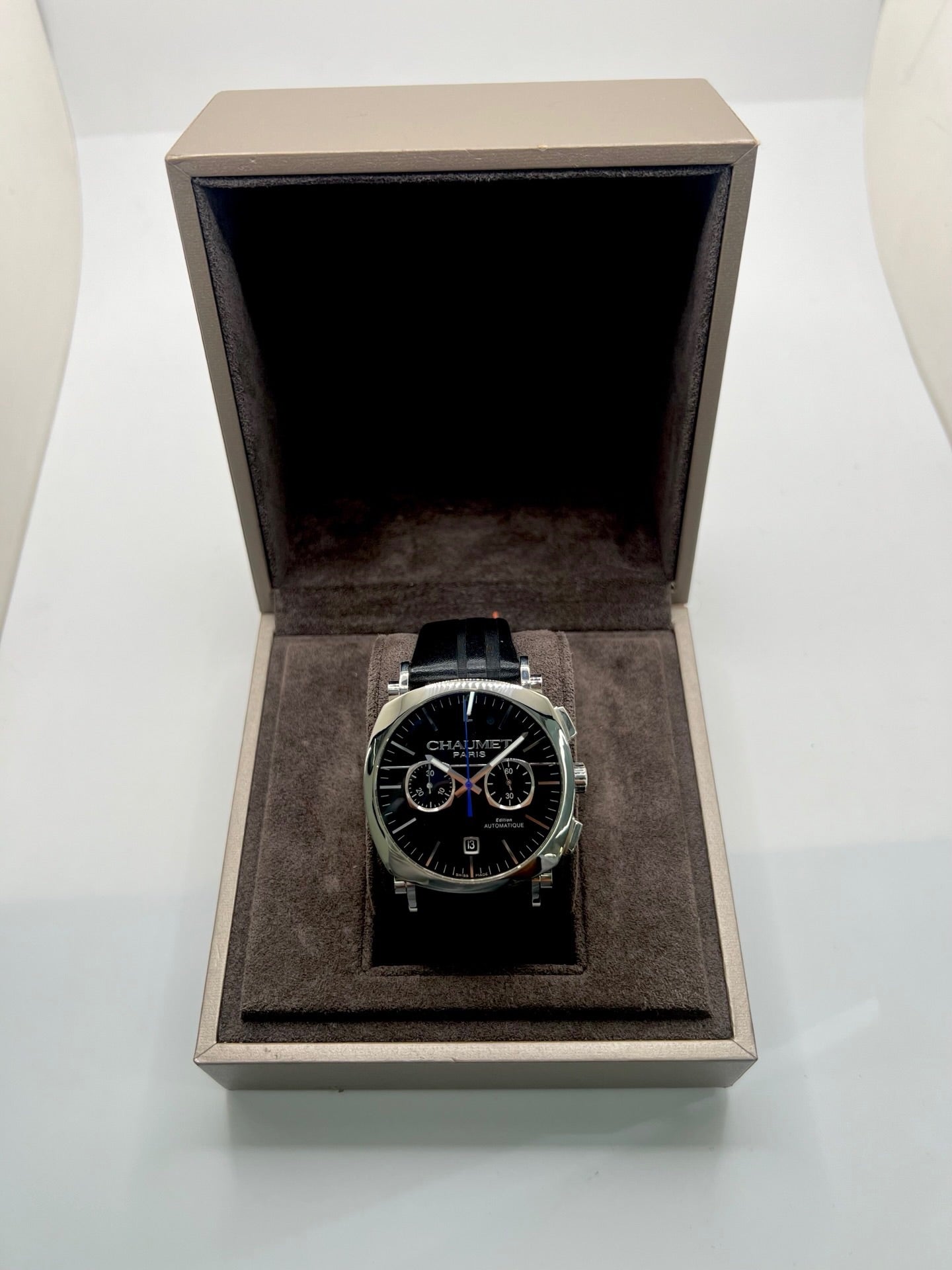 Montre Chaumet Dandy réf. 1229 pour homme ou unisexe, dotée d’un mouvement automatique. Boîtier en acier de 40 mm avec lunette assortie et verre saphir résistant aux rayures. Cadran noir à index bâtons, fonction chronographe et affichage de la date. Bracelet en cuir noir avec boucle déployante en acier. Montre de luxe d’occasion en très bon état, présentant de légères traces d’usure. Révisée en interne le 23 juin 2026, livrée avec coffret d’origine, sans papiers. Disponible à Paris. 