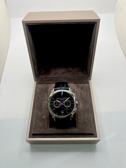 Montre Chaumet Dandy réf. 1229 pour homme ou unisexe, dotée d’un mouvement automatique. Boîtier en acier de 40 mm avec lunette assortie et verre saphir résistant aux rayures. Cadran noir à index bâtons, fonction chronographe et affichage de la date. Bracelet en cuir noir avec boucle déployante en acier. Montre de luxe d’occasion en très bon état, présentant de légères traces d’usure. Révisée en interne le 23 juin 2026, livrée avec coffret d’origine, sans papiers. Disponible à Paris. 