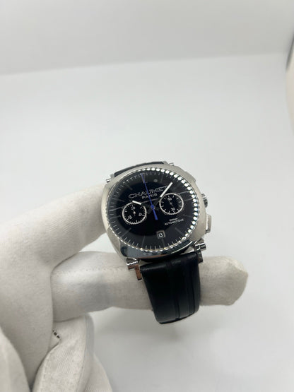 Montre Chaumet Dandy réf. 1229 pour homme ou unisexe, dotée d’un mouvement automatique. Boîtier en acier de 40 mm avec lunette assortie et verre saphir résistant aux rayures. Cadran noir à index bâtons, fonction chronographe et affichage de la date. Bracelet en cuir noir avec boucle déployante en acier. Montre de luxe d’occasion en très bon état, présentant de légères traces d’usure. Révisée en interne le 23 juin 2026, livrée avec coffret d’origine, sans papiers. Disponible à Paris. 