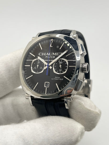 Montre Chaumet Dandy réf. 1229 pour homme ou unisexe, dotée d’un mouvement automatique. Boîtier en acier de 40 mm avec lunette assortie et verre saphir résistant aux rayures. Cadran noir à index bâtons, fonction chronographe et affichage de la date. Bracelet en cuir noir avec boucle déployante en acier. Montre de luxe d’occasion en très bon état, présentant de légères traces d’usure. Révisée en interne le 23 juin 2026, livrée avec coffret d’origine, sans papiers. Disponible à Paris. 
