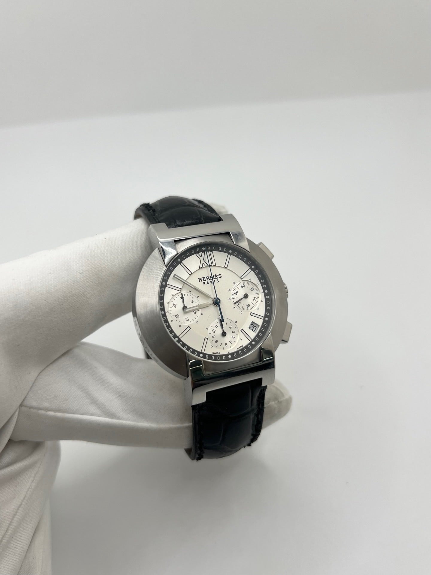 Montre Hermès Nomade Chronograph en acier avec boîtier de 39 mm et cadran blanc à index bâtons. Ce chronographe à mouvement quartz est équipé d’un verre saphir, d’un affichage de la date et d’un bracelet en cuir de crocodile gris avec boucle déployante en acier. Son design élégant et sportif reflète le savoir-faire horloger de la maison Hermès. Modèle unisexe d’occasion en très bon état, alliant confort, précision et raffinement au quotidien.
