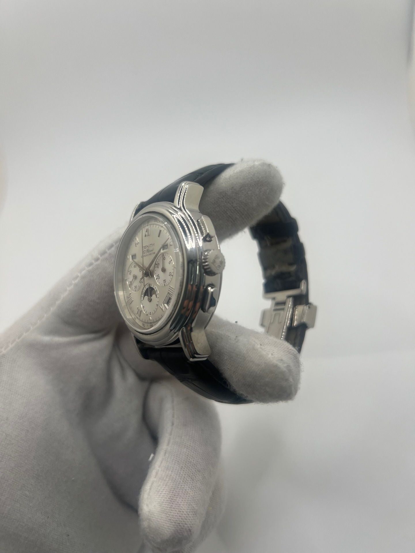 Montre chronographe automatique en acier avec cadran argenté à chiffres romains, fonction phase lunaire, date, jour et mois. Boîtier de 40 mm, verre saphir, fond transparent et bracelet en cuir noir. Modèle de haute précision doté du calibre 410 avec 50 heures de réserve de marche. Montre élégante pour homme ou unisexe.