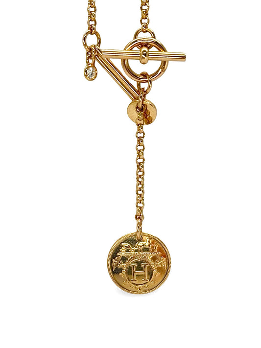 Collier en or rose 18 carats au design circulaire inspiré des codes équestres, symbole d’élégance et de raffinement. Pendentif ajouré suspendu à une chaîne fine, offrant une silhouette équilibrée et contemporaine. Bijou précieux au style intemporel, idéal à porter seul ou en accumulation, apportant une touche lumineuse et sophistiquée à toutes les tenues, du quotidien aux occasions spéciales.