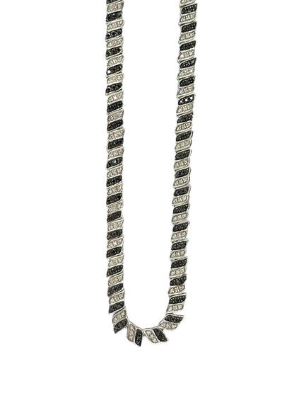 Élégant collier en or blanc 18 carats sublimé par des diamants noirs et incolores totalisant 2 carats. Un bijou raffiné qui joue sur le contraste entre lumière et obscurité, symbole de sophistication et d’élégance intemporelle, idéal pour sublimer toutes les tenues avec éclat et modernité.