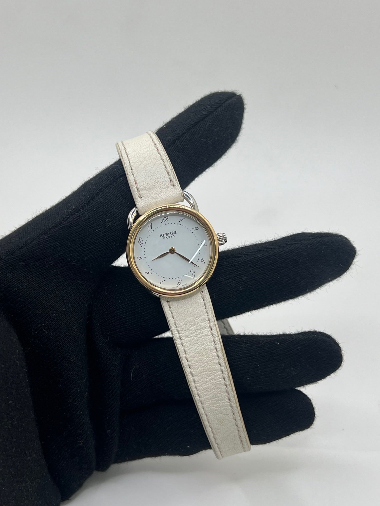 Élégante montre Hermès Arceau pour femme, boîtier en or et acier, cadran blanc aux chiffres arabes et bracelet en cuir beige. Ce garde-temps emblématique allie raffinement et savoir-faire horloger français, offrant un design intemporel et une précision quartz idéale pour un style classique et chic.