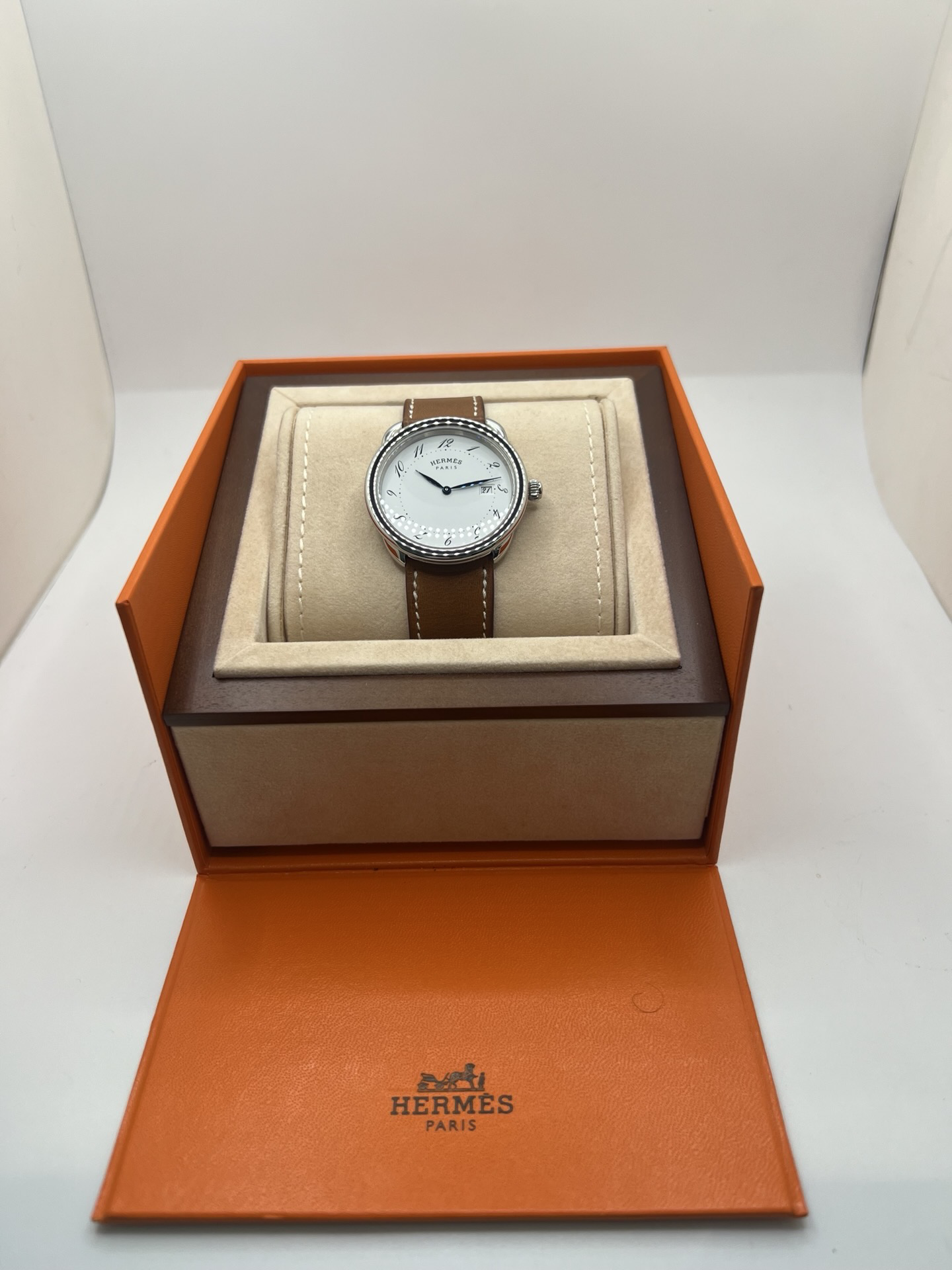 Montre Hermès Arceau Grand Modèle AR5.710 de 2014 en acier 38 mm avec mouvement quartz, cadran blanc à chiffres arabes et bracelet cuir brun d’origine. Cette montre de luxe Hermès Full Set avec boîte et papiers possède un verre saphir, une boucle ardillon acier et le design emblématique Arceau inspiré de l’univers équestre. Montre vintage Hermès élégante, révisée en 2026 et garantie 1 an.