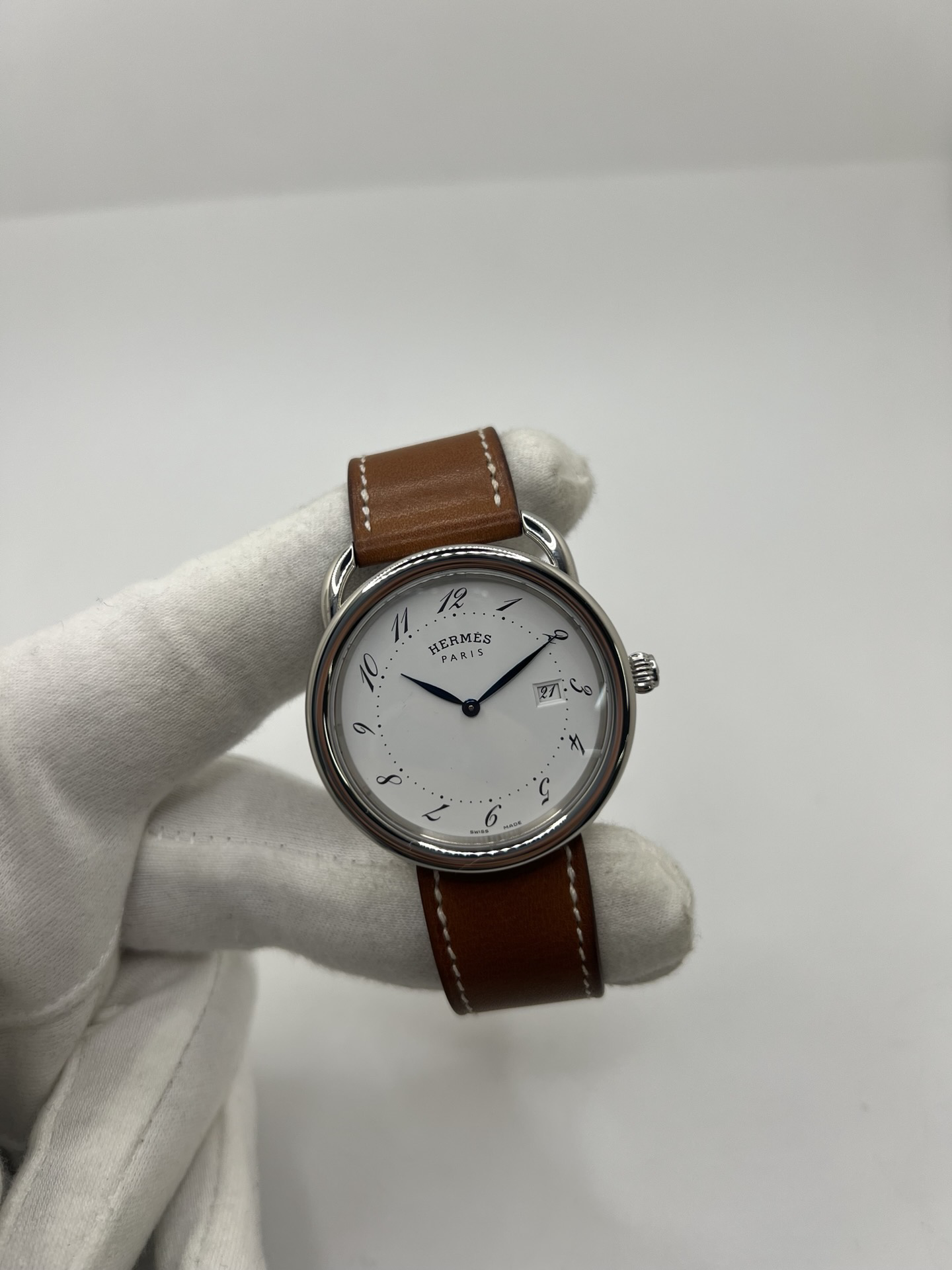 Montre Hermès Arceau Grand Modèle AR5.710 de 2014 en acier 38 mm avec mouvement quartz, cadran blanc à chiffres arabes et bracelet cuir brun d’origine. Cette montre de luxe Hermès Full Set avec boîte et papiers possède un verre saphir, une boucle ardillon acier et le design emblématique Arceau inspiré de l’univers équestre. Montre vintage Hermès élégante, révisée en 2026 et garantie 1 an.