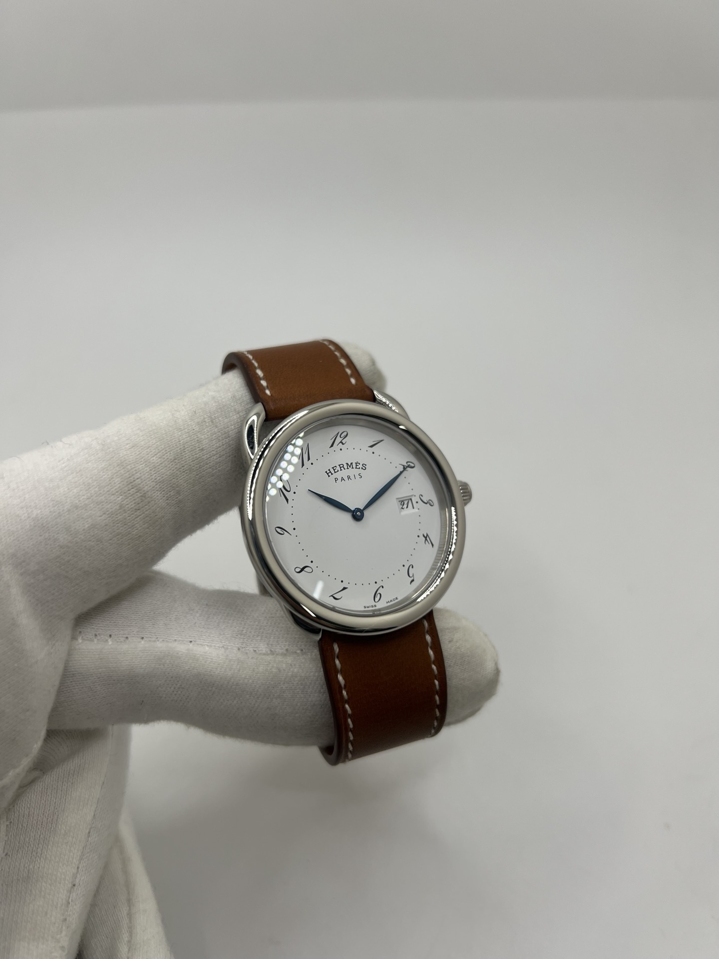 Montre Hermès Arceau Grand Modèle AR5.710 de 2014 en acier 38 mm avec mouvement quartz, cadran blanc à chiffres arabes et bracelet cuir brun d’origine. Cette montre de luxe Hermès Full Set avec boîte et papiers possède un verre saphir, une boucle ardillon acier et le design emblématique Arceau inspiré de l’univers équestre. Montre vintage Hermès élégante, révisée en 2026 et garantie 1 an.