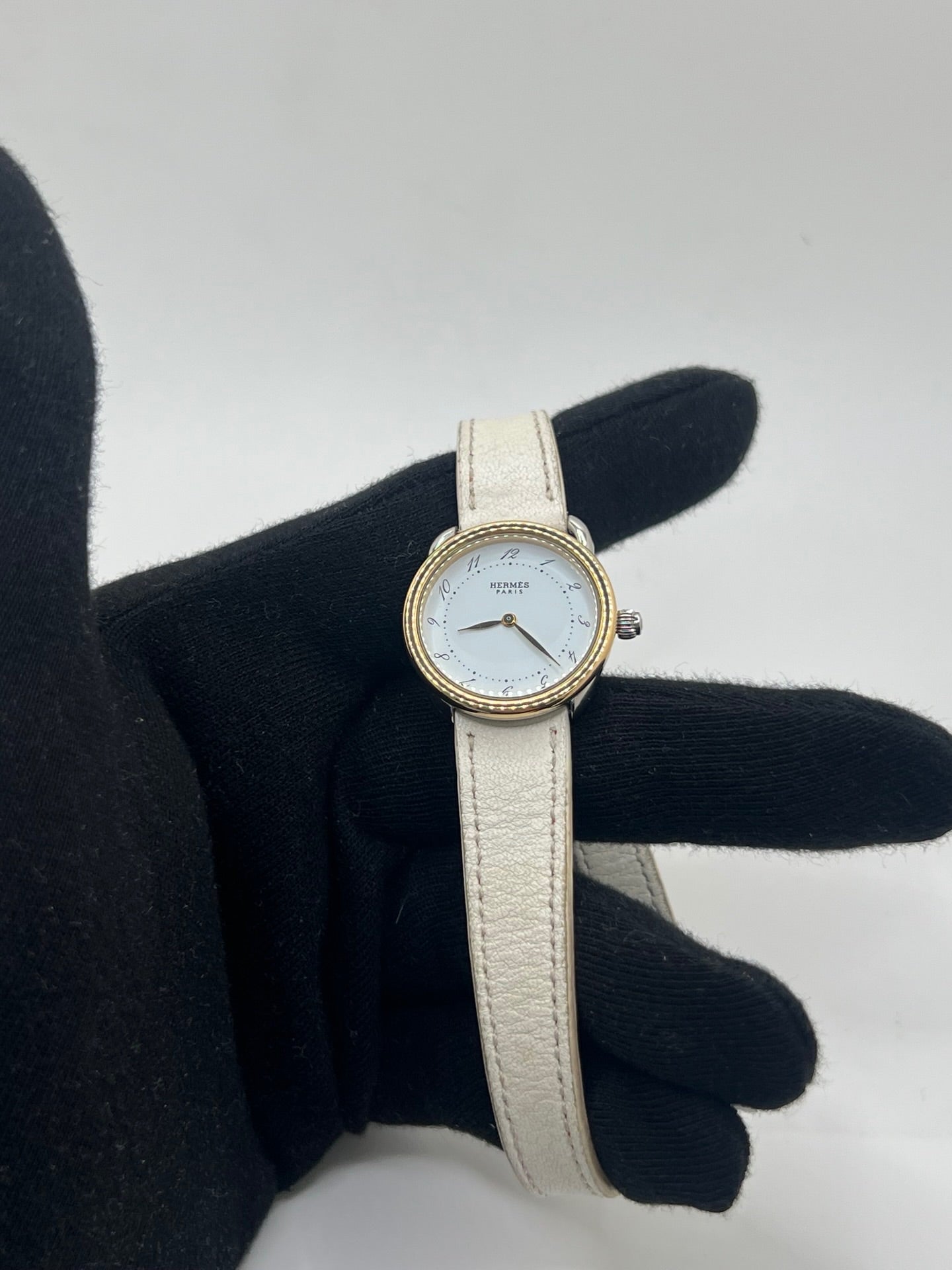 Élégante montre Hermès Arceau pour femme, boîtier en or et acier, cadran blanc aux chiffres arabes et bracelet en cuir beige. Ce garde-temps emblématique allie raffinement et savoir-faire horloger français, offrant un design intemporel et une précision quartz idéale pour un style classique et chic.