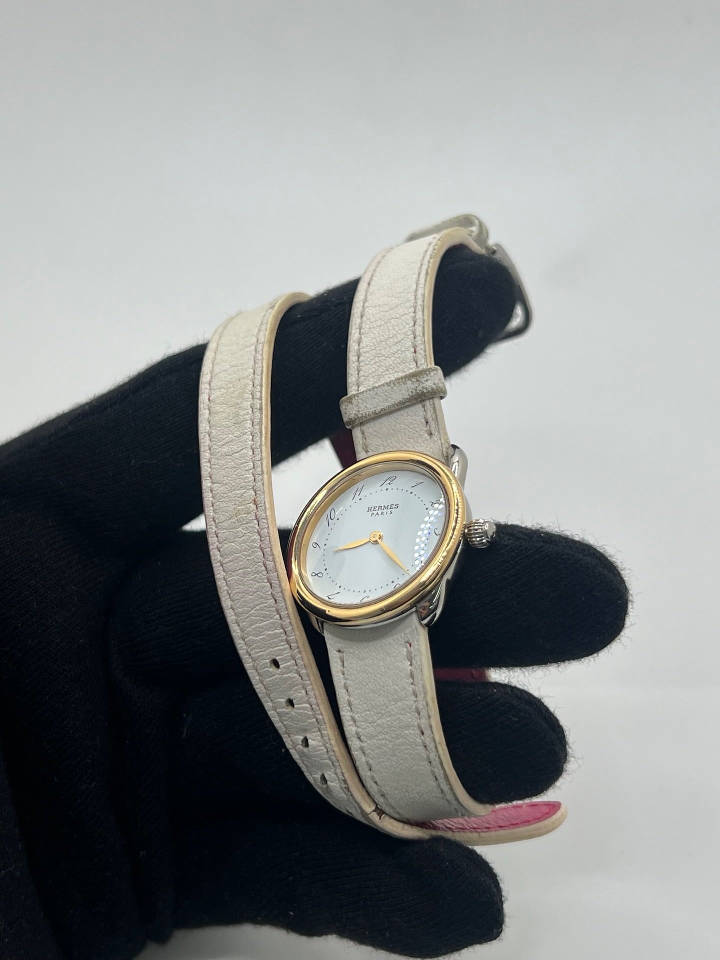 Élégante montre Hermès Arceau pour femme, boîtier en or et acier, cadran blanc aux chiffres arabes et bracelet en cuir beige. Ce garde-temps emblématique allie raffinement et savoir-faire horloger français, offrant un design intemporel et une précision quartz idéale pour un style classique et chic.
