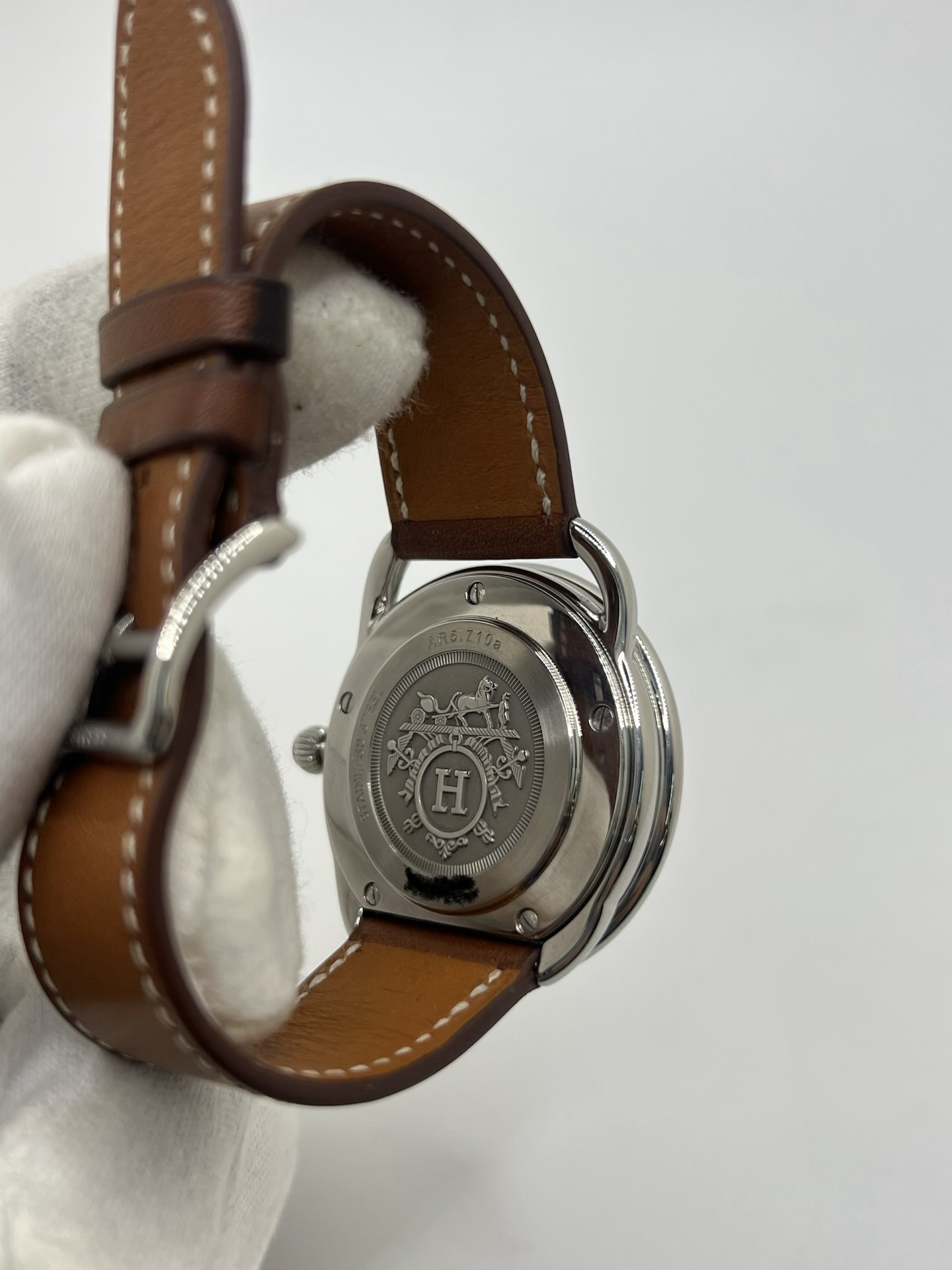 Montre Hermès Arceau Grand Modèle AR5.710 de 2014 en acier 38 mm avec mouvement quartz, cadran blanc à chiffres arabes et bracelet cuir brun d’origine. Cette montre de luxe Hermès Full Set avec boîte et papiers possède un verre saphir, une boucle ardillon acier et le design emblématique Arceau inspiré de l’univers équestre. Montre vintage Hermès élégante, révisée en 2026 et garantie 1 an.