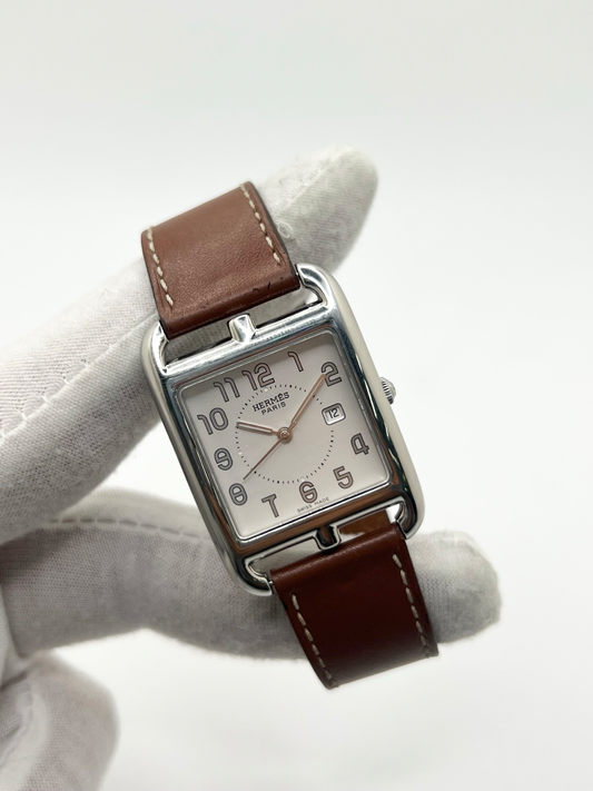 Montre Hermès Cape Cod Grand Modèle en acier inoxydable, boîtier rectangulaire iconique aux lignes élégantes et contemporaines, cadran argenté épuré avec chiffres arabes stylisés et aiguilles fines. Bracelet en cuir signature Hermès offrant confort et raffinement. Mouvement quartz précis. Montre de luxe intemporelle et sophistiquée, idéale pour un porté quotidien ou une tenue habillée, symbole du savoir-faire horloger et du style parisien.
