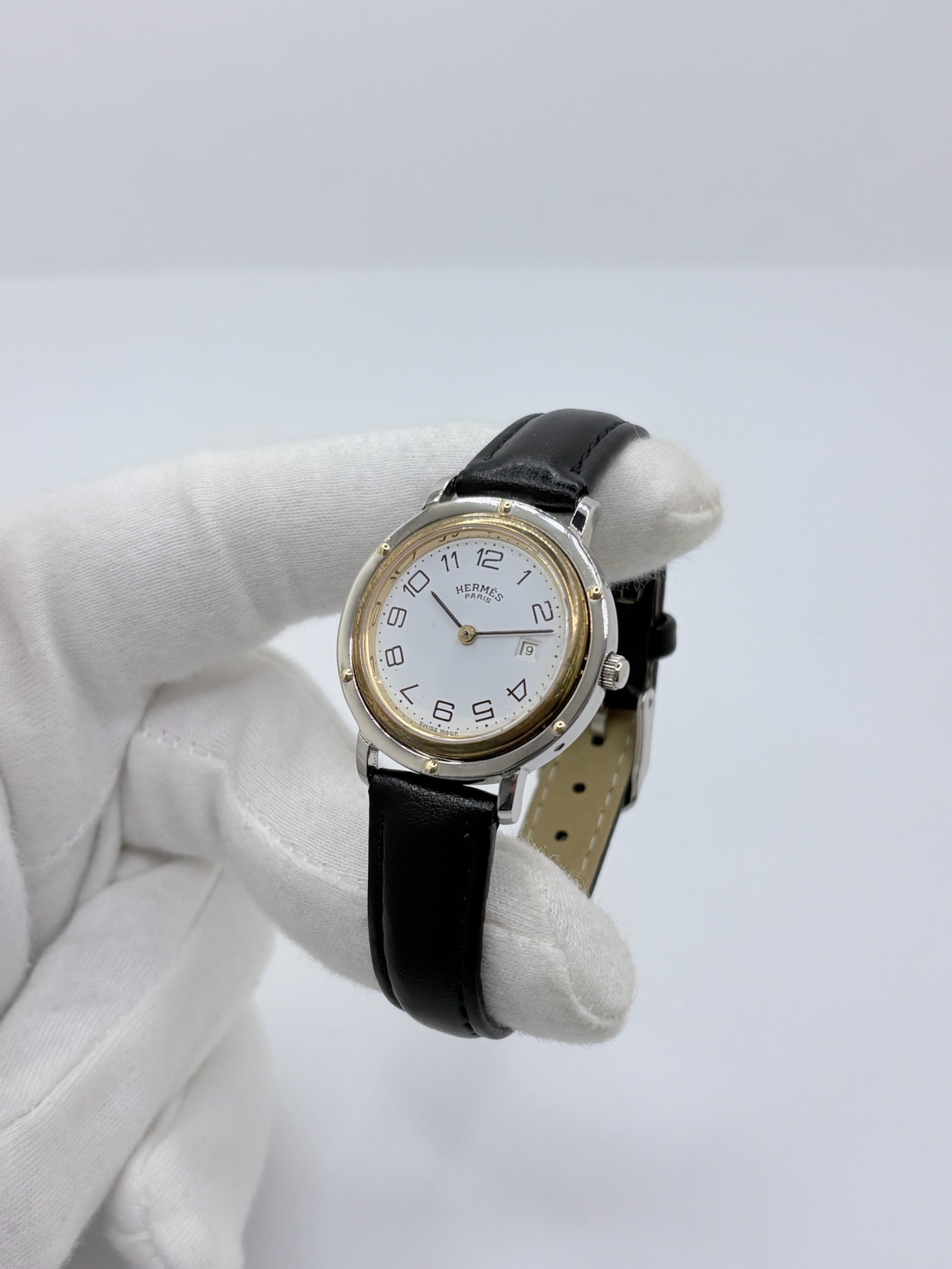 Montre Hermès Clipper pour femme en acier, équipée d’un mouvement à quartz. Son boîtier de 30 mm est associé à une lunette en or jaune, un cadran blanc avec chiffres arabes et un verre saphir. Cette montre Hermès Clipper est montée sur un bracelet en cuir de vache noir avec boucle ardillon en acier. Un modèle élégant et intemporel de la collection Clipper, idéal pour les amateurs de montres de luxe.