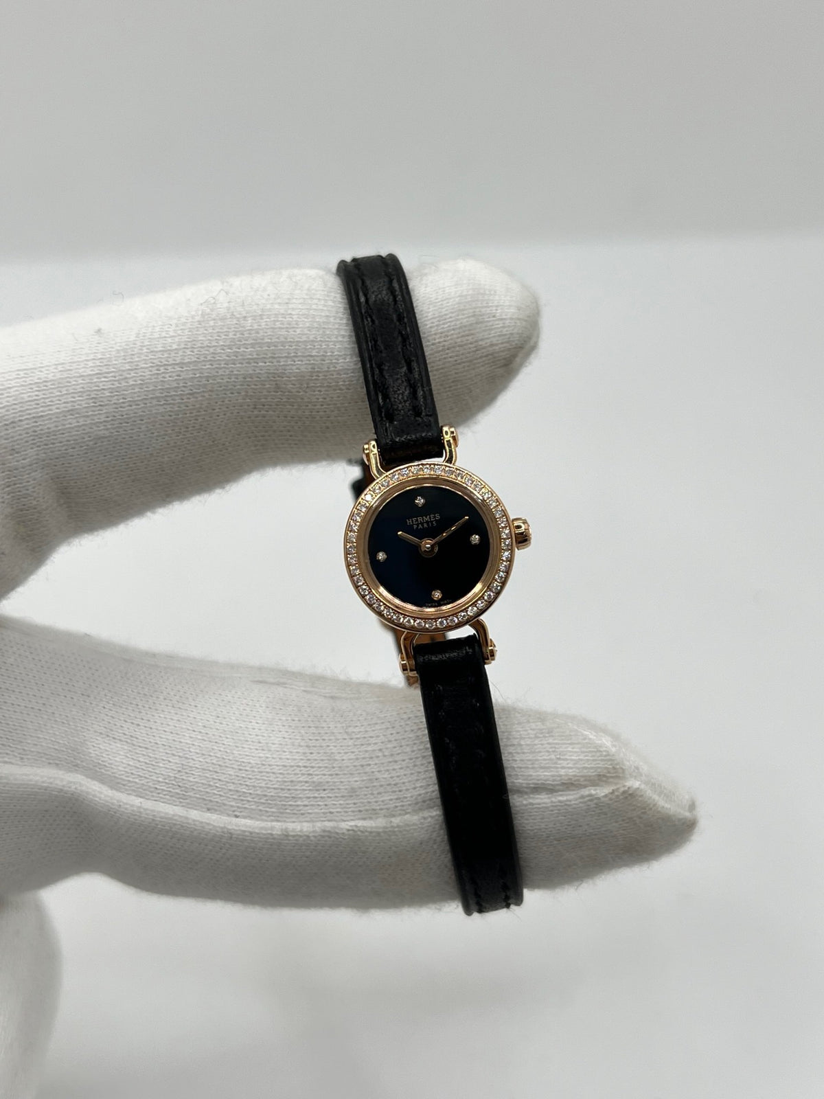 Montre Hermès Faubourg FG4.171 pour femme, dotée d’un élégant boîtier en or rose de 15,5 mm et d’un mouvement quartz. Elle se distingue par son cadran noir sans chiffres, protégé par un verre saphir, et son bracelet en cuir noir avec boucle ardillon en or rose. Cette montre de luxe Hermès associe raffinement, élégance et discrétion. Modèle d’occasion en très bon état, révisé en interne en octobre 2026 et livré avec son coffret d’origine.