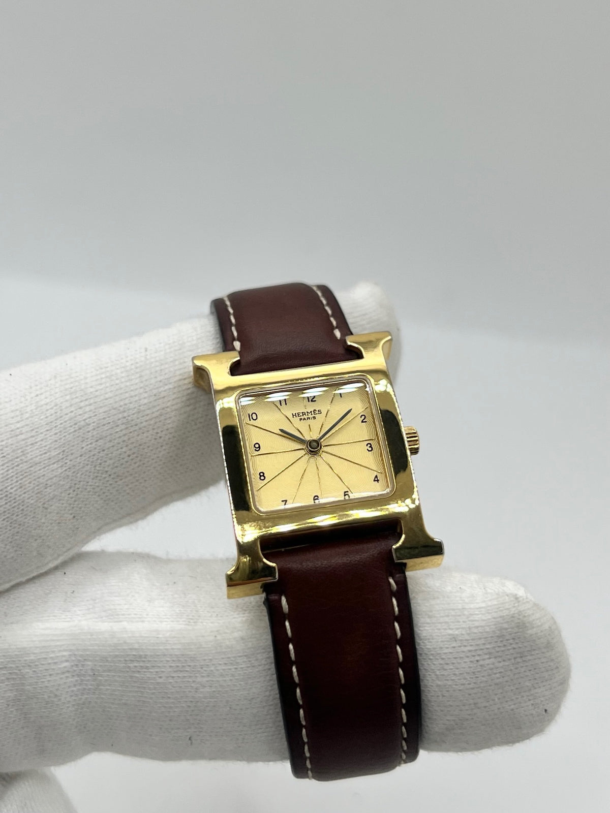 Montre Hermès Heure H HH1.201 pour femme, équipée d’un mouvement quartz et d’un boîtier en acier de 21 mm. Son cadran couleur or est protégé par un verre saphir et accompagné d’un bracelet brun en cuir de vache avec boucle ardillon en acier. Étanche à 3 ATM, cette montre Hermès Heure H se distingue par son célèbre boîtier en forme de H et son design élégant. En très bon état, elle présente de légères traces d’usure.
