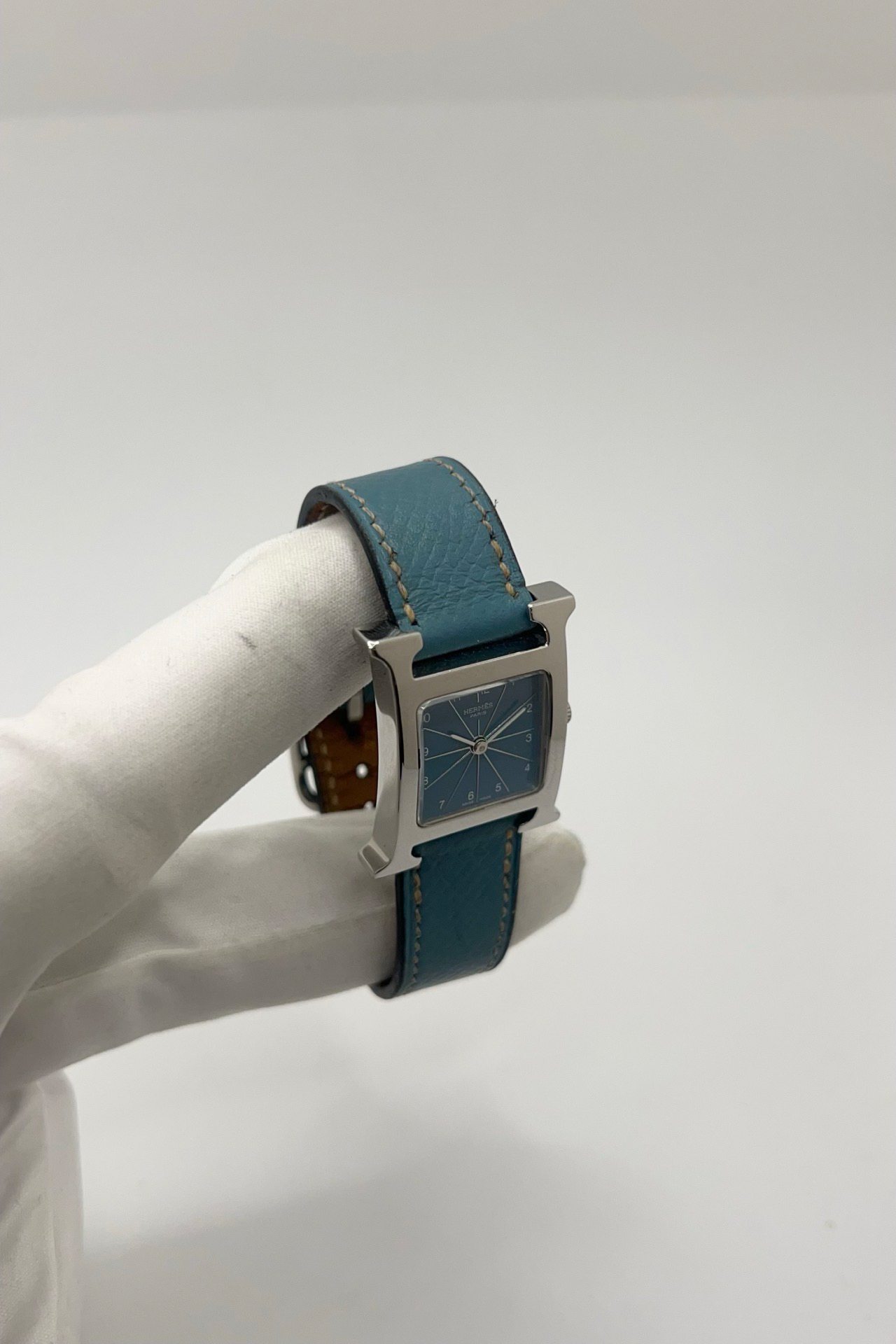 Montre Hermès Heure H HH1.210 en acier avec cadran bleu à chiffres arabes et bracelet cuir Hermès bleu d’origine. Cette montre Hermès femme quartz au design iconique en forme de H incarne l’élégance parisienne et le luxe discret. Modèle Hermès Heure H acier de 21 x 30 mm avec verre saphir, boucle ardillon acier et mouvement quartz fiable. Montre de luxe féminine chic et intemporelle, révisée et livrée avec certificat d’authenticité.