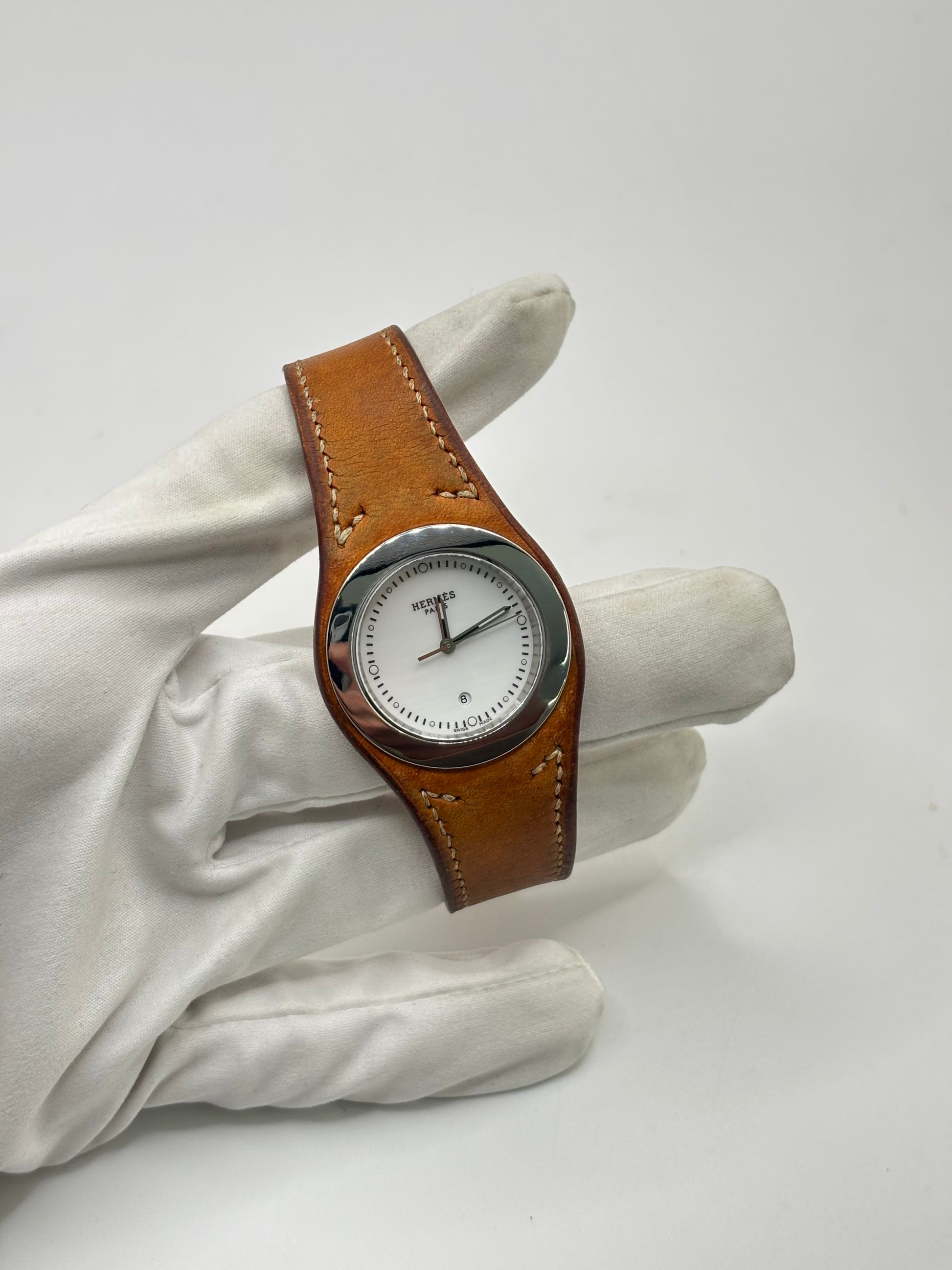 Montre Hermès Harnais HA3.410 en acier avec mouvement quartz, cadran blanc et bracelet en cuir brun. Modèle homme et unisexe au design élégant avec verre saphir et fonction date. Montre d’occasion en très bon état avec légères traces d’usure et micro-rayures discrètes. Format 30 mm idéal pour un style classique et raffiné.
