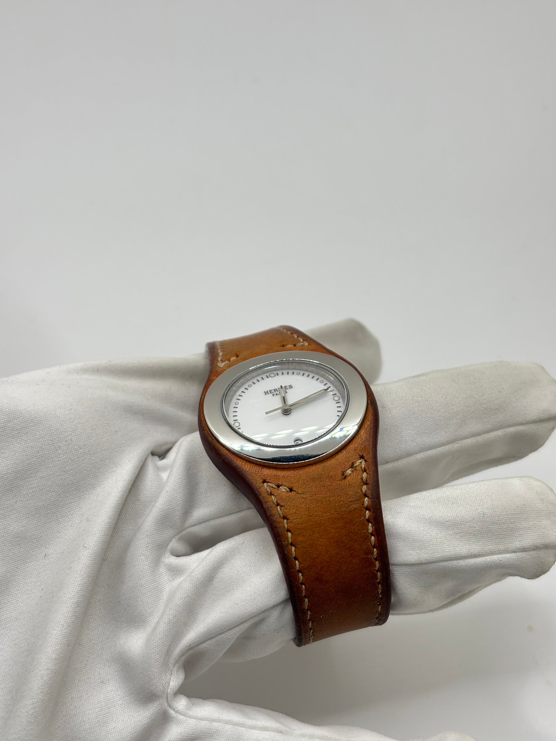 Montre Hermès Harnais HA3.410 en acier avec mouvement quartz, cadran blanc et bracelet en cuir brun. Modèle homme et unisexe au design élégant avec verre saphir et fonction date. Montre d’occasion en très bon état avec légères traces d’usure et micro-rayures discrètes. Format 30 mm idéal pour un style classique et raffiné.
