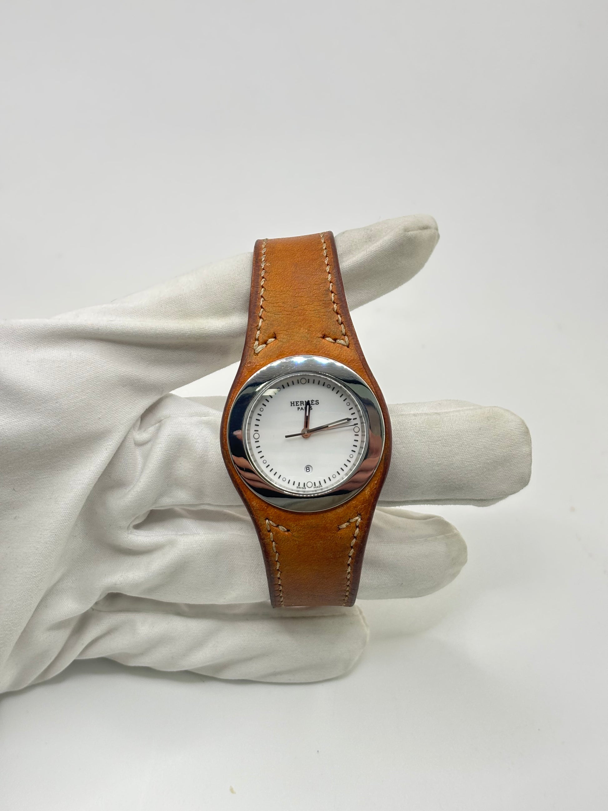 Montre Hermès Harnais HA3.410 en acier avec mouvement quartz, cadran blanc et bracelet en cuir brun. Modèle homme et unisexe au design élégant avec verre saphir et fonction date. Montre d’occasion en très bon état avec légères traces d’usure et micro-rayures discrètes. Format 30 mm idéal pour un style classique et raffiné.
