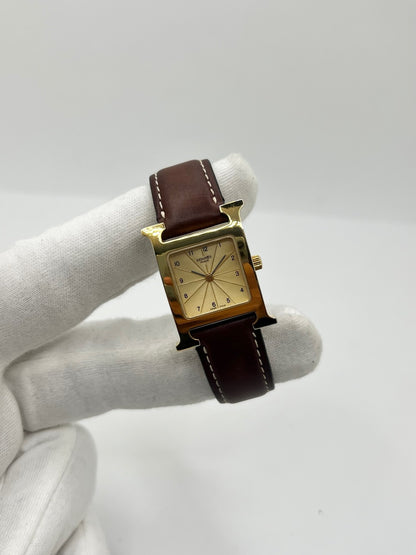 Montre Hermès Heure H HH1.201 pour femme, équipée d’un mouvement quartz et d’un boîtier en acier de 21 mm. Son cadran couleur or est protégé par un verre saphir et accompagné d’un bracelet brun en cuir de vache avec boucle ardillon en acier. Étanche à 3 ATM, cette montre Hermès Heure H se distingue par son célèbre boîtier en forme de H et son design élégant. En très bon état, elle présente de légères traces d’usure.
