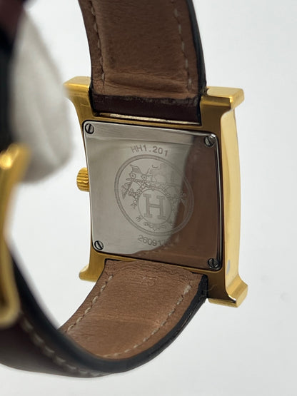 Montre Hermès Heure H HH1.201 pour femme, équipée d’un mouvement quartz et d’un boîtier en acier de 21 mm. Son cadran couleur or est protégé par un verre saphir et accompagné d’un bracelet brun en cuir de vache avec boucle ardillon en acier. Étanche à 3 ATM, cette montre Hermès Heure H se distingue par son célèbre boîtier en forme de H et son design élégant. En très bon état, elle présente de légères traces d’usure.
