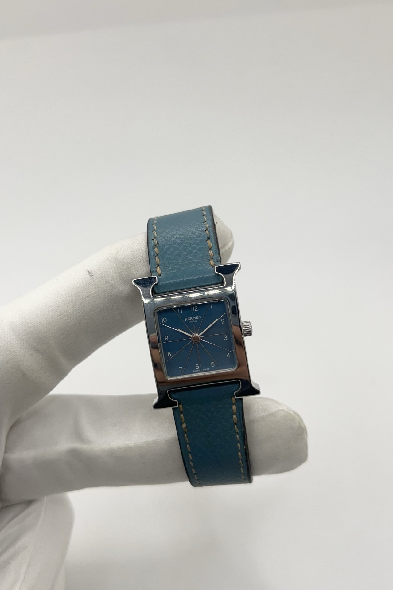 Montre Hermès Heure H HH1.210 en acier avec cadran bleu à chiffres arabes et bracelet cuir Hermès bleu d’origine. Cette montre Hermès femme quartz au design iconique en forme de H incarne l’élégance parisienne et le luxe discret. Modèle Hermès Heure H acier de 21 x 30 mm avec verre saphir, boucle ardillon acier et mouvement quartz fiable. Montre de luxe féminine chic et intemporelle, révisée et livrée avec certificat d’authenticité.