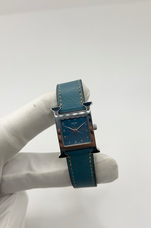 Montre Hermès Heure H HH1.210 en acier avec cadran bleu à chiffres arabes et bracelet cuir Hermès bleu d’origine. Cette montre Hermès femme quartz au design iconique en forme de H incarne l’élégance parisienne et le luxe discret. Modèle Hermès Heure H acier de 21 x 30 mm avec verre saphir, boucle ardillon acier et mouvement quartz fiable. Montre de luxe féminine chic et intemporelle, révisée et livrée avec certificat d’authenticité.