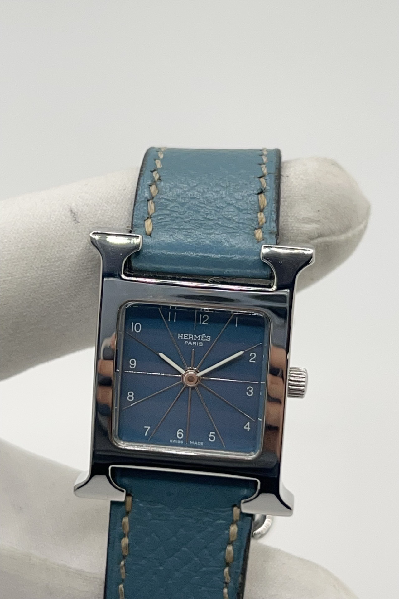 Montre Hermès Heure H HH1.210 en acier avec cadran bleu à chiffres arabes et bracelet cuir Hermès bleu d’origine. Cette montre Hermès femme quartz au design iconique en forme de H incarne l’élégance parisienne et le luxe discret. Modèle Hermès Heure H acier de 21 x 30 mm avec verre saphir, boucle ardillon acier et mouvement quartz fiable. Montre de luxe féminine chic et intemporelle, révisée et livrée avec certificat d’authenticité.