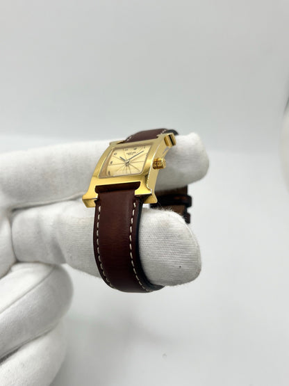Montre Hermès Heure H HH1.201 pour femme, équipée d’un mouvement quartz et d’un boîtier en acier de 21 mm. Son cadran couleur or est protégé par un verre saphir et accompagné d’un bracelet brun en cuir de vache avec boucle ardillon en acier. Étanche à 3 ATM, cette montre Hermès Heure H se distingue par son célèbre boîtier en forme de H et son design élégant. En très bon état, elle présente de légères traces d’usure.
