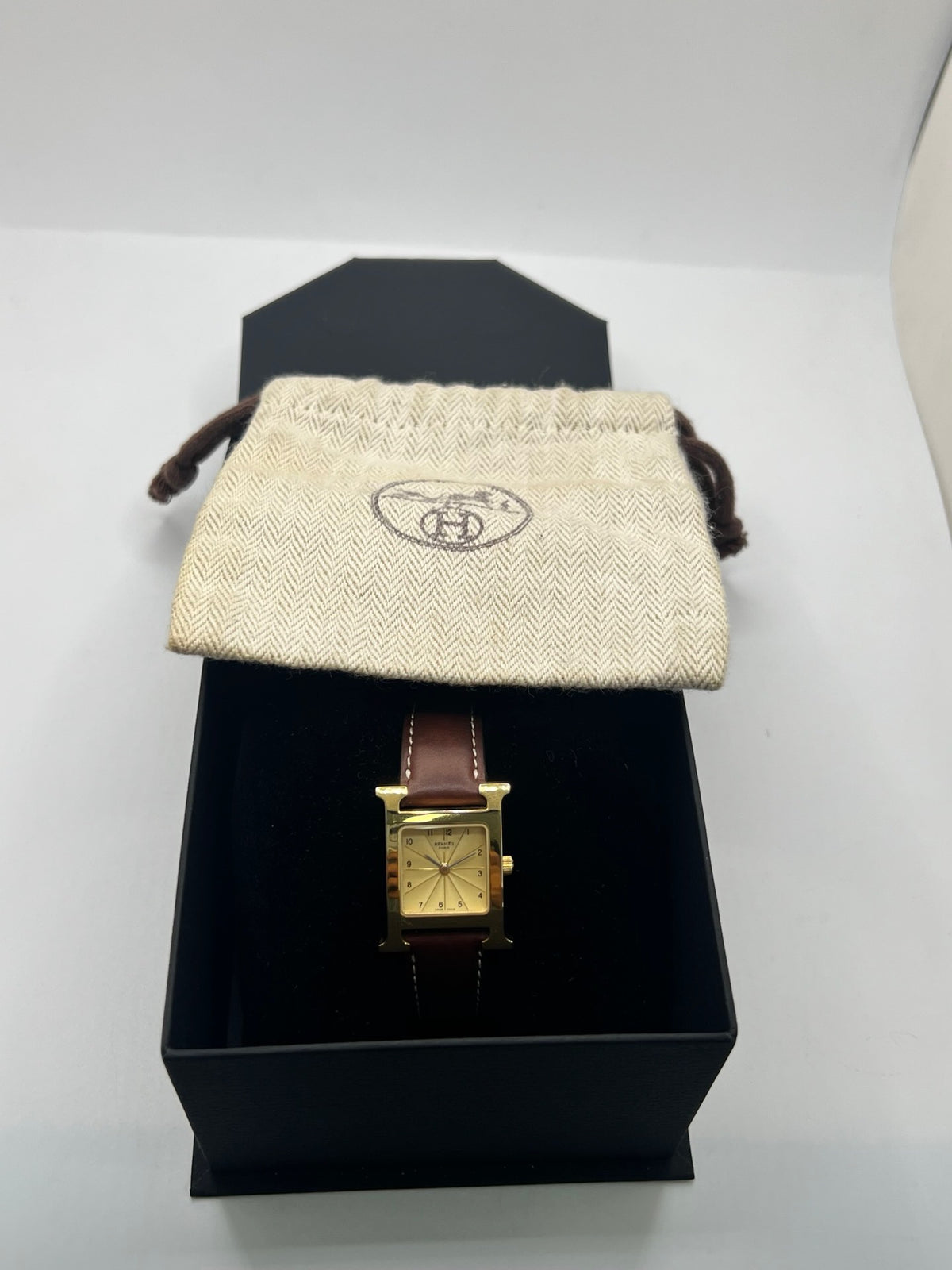 Montre Hermès Heure H HH1.201 pour femme, équipée d’un mouvement quartz et d’un boîtier en acier de 21 mm. Son cadran couleur or est protégé par un verre saphir et accompagné d’un bracelet brun en cuir de vache avec boucle ardillon en acier. Étanche à 3 ATM, cette montre Hermès Heure H se distingue par son célèbre boîtier en forme de H et son design élégant. En très bon état, elle présente de légères traces d’usure.
