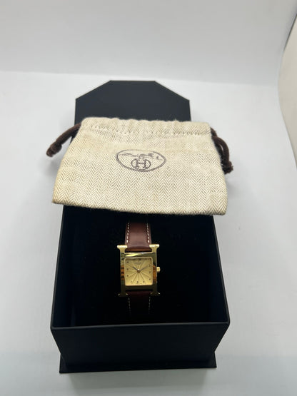 Montre Hermès Heure H HH1.201 pour femme, équipée d’un mouvement quartz et d’un boîtier en acier de 21 mm. Son cadran couleur or est protégé par un verre saphir et accompagné d’un bracelet brun en cuir de vache avec boucle ardillon en acier. Étanche à 3 ATM, cette montre Hermès Heure H se distingue par son célèbre boîtier en forme de H et son design élégant. En très bon état, elle présente de légères traces d’usure.
