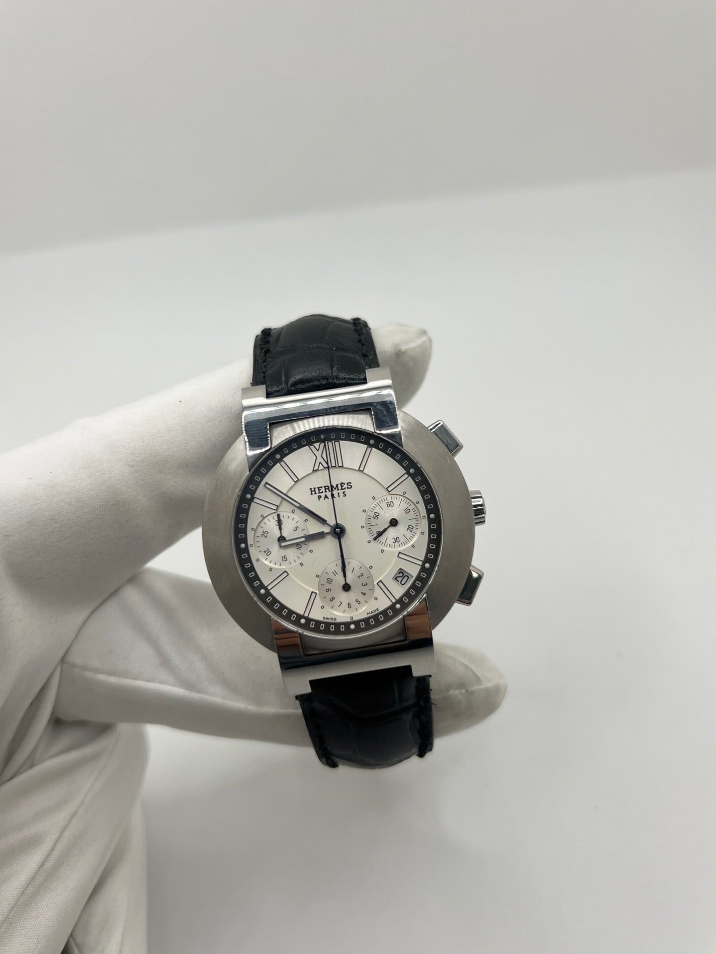 Montre Hermès Nomade Chronograph en acier avec boîtier de 39 mm et cadran blanc à index bâtons. Ce chronographe à mouvement quartz est équipé d’un verre saphir, d’un affichage de la date et d’un bracelet en cuir de crocodile gris avec boucle déployante en acier. Son design élégant et sportif reflète le savoir-faire horloger de la maison Hermès. Modèle unisexe d’occasion en très bon état, alliant confort, précision et raffinement au quotidien.
