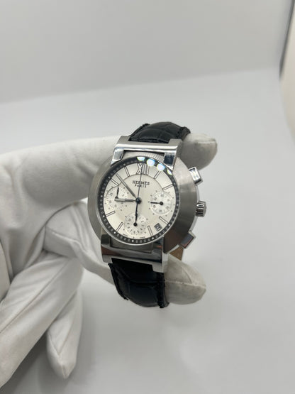 Montre Hermès Nomade Chronograph en acier avec boîtier de 39 mm et cadran blanc à index bâtons. Ce chronographe à mouvement quartz est équipé d’un verre saphir, d’un affichage de la date et d’un bracelet en cuir de crocodile gris avec boucle déployante en acier. Son design élégant et sportif reflète le savoir-faire horloger de la maison Hermès. Modèle unisexe d’occasion en très bon état, alliant confort, précision et raffinement au quotidien.
